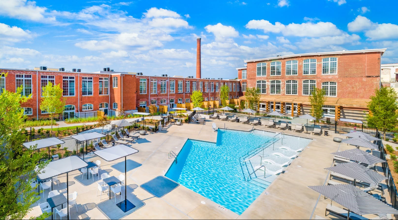 The property’s outdoor amenities offer a striking contrast to its industrial interiors, with a resort-style pool surrounded by seating and the historic mill buildings. | Source: Facebook/Judson Mills Loft