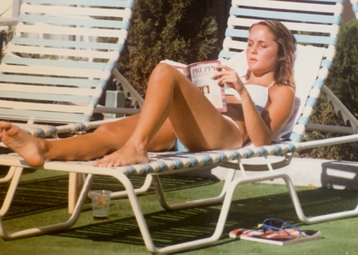 A 16-year-old Erin Murphy stretched out on a lounge chair while working on her tan and reading "The Preppy Handbook." The casual snapshot shows the former "Bewitched" child star in her teen years, years before the polished 2026 selfies that reignited interest in her changing look. | Source: Instagram/erinmurphybewitched
