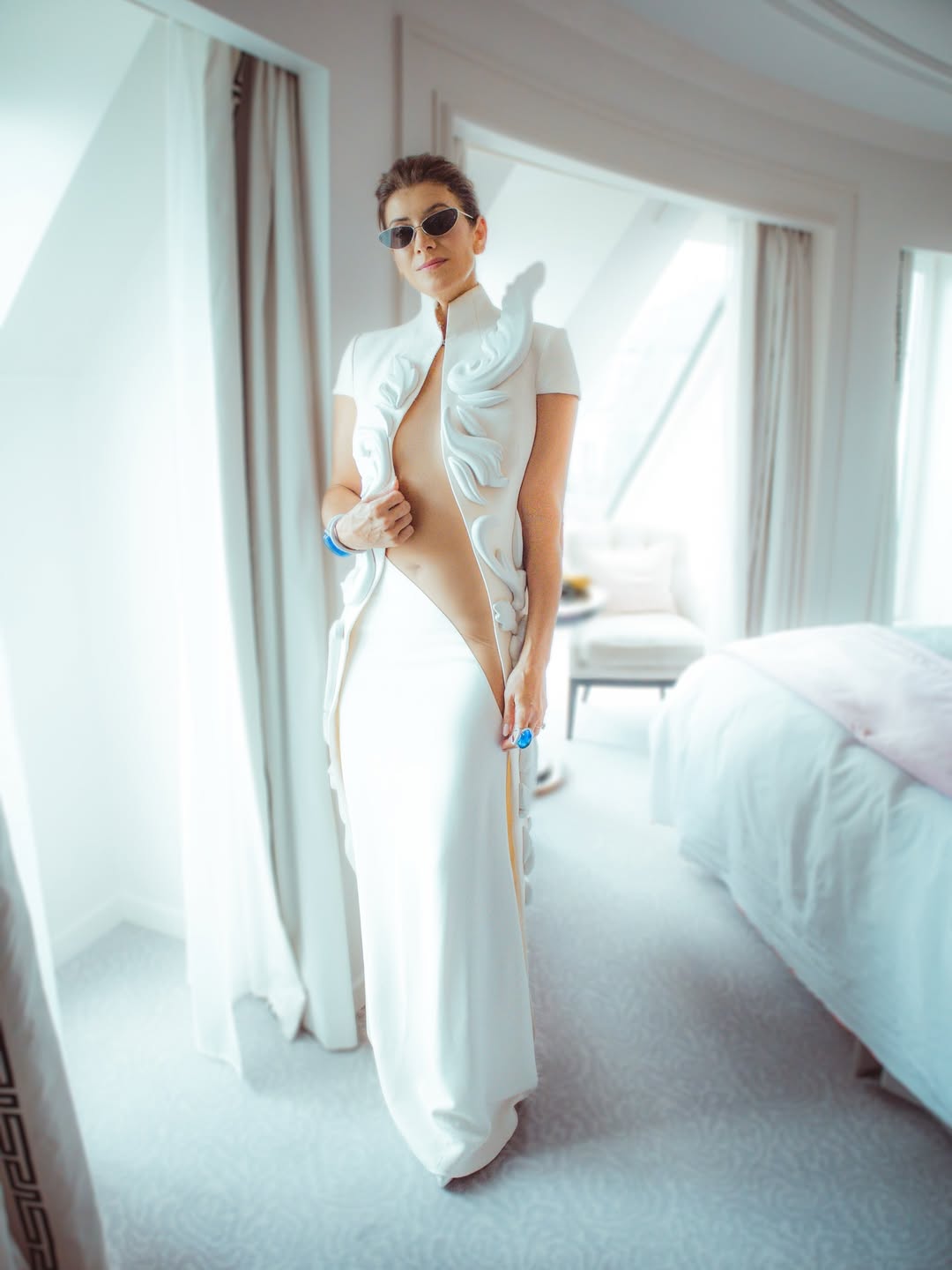 Kate Walsh poses by a window in her striking white cut-out gown, styled with tinted sunglasses | Source: Instagram/katewalsh