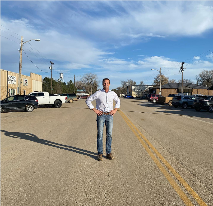 Bryon Noem stands centered on a quiet small-town road, hands on hips—framed by open sky and everyday storefronts, steady and self-assured. | Source: Instagram/sdbryonnoem