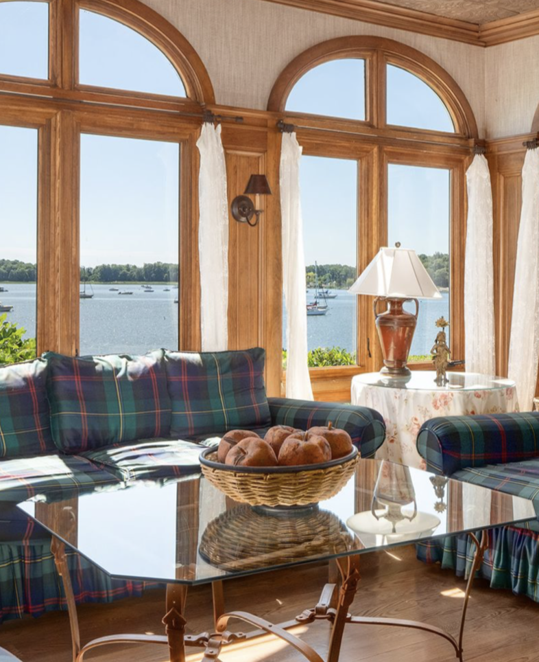 Inside Kathie Lee's Connecticut estate, plaid sofas, warm wooden details, and arched windows create a cozy, traditional atmosphere. The room overlooks Long Island Sound, offering beautiful views of the water and passing sailboats. | Source: Instagram/@ robbreport