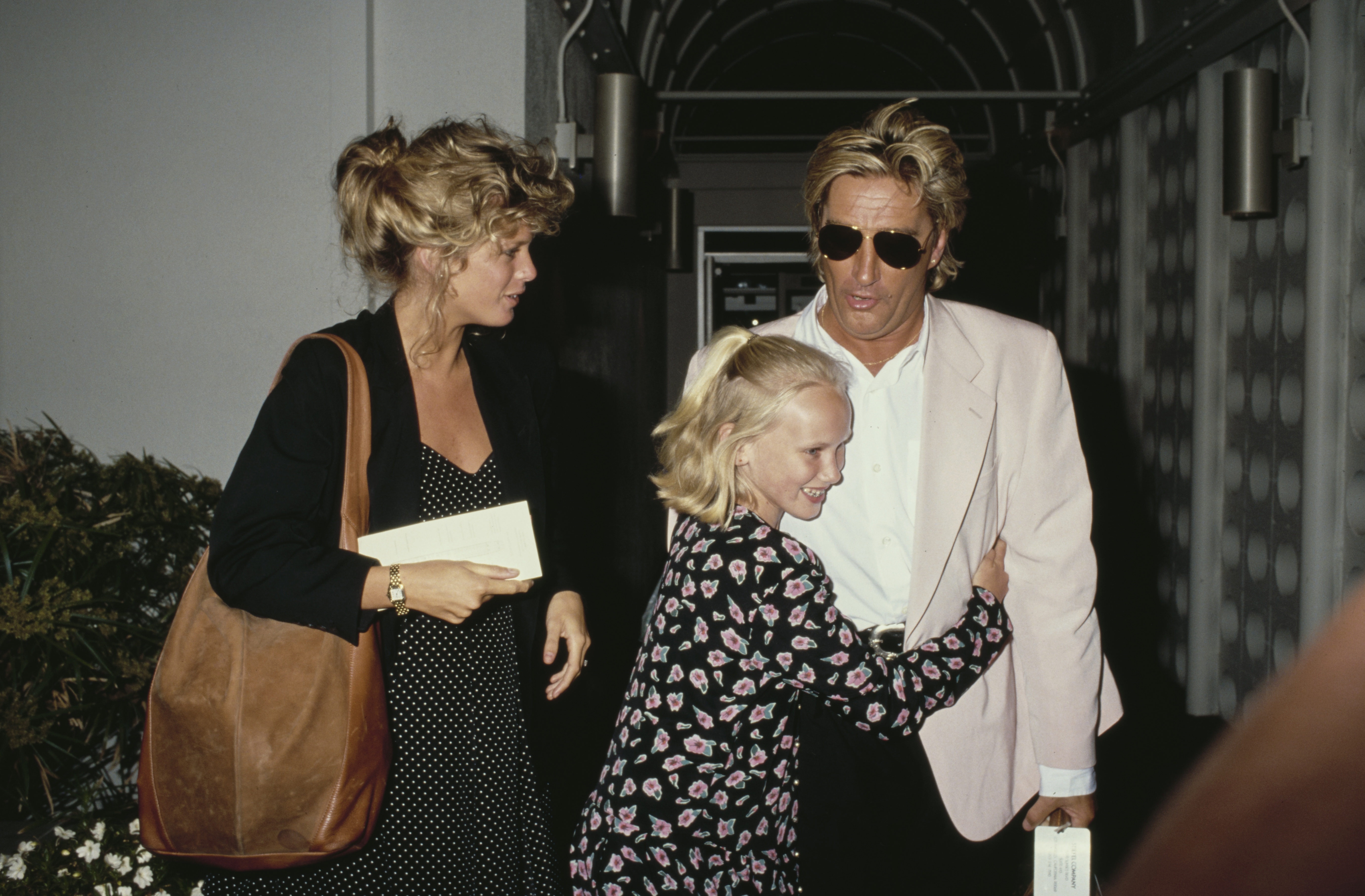 New Zealand model Rachel Hunter, Kimberly Stewart, and British singer and songwriter Rod Stewart embrace at Los Angeles International Airport in Los Angeles, California, circa 1990. | Source: Getty Images