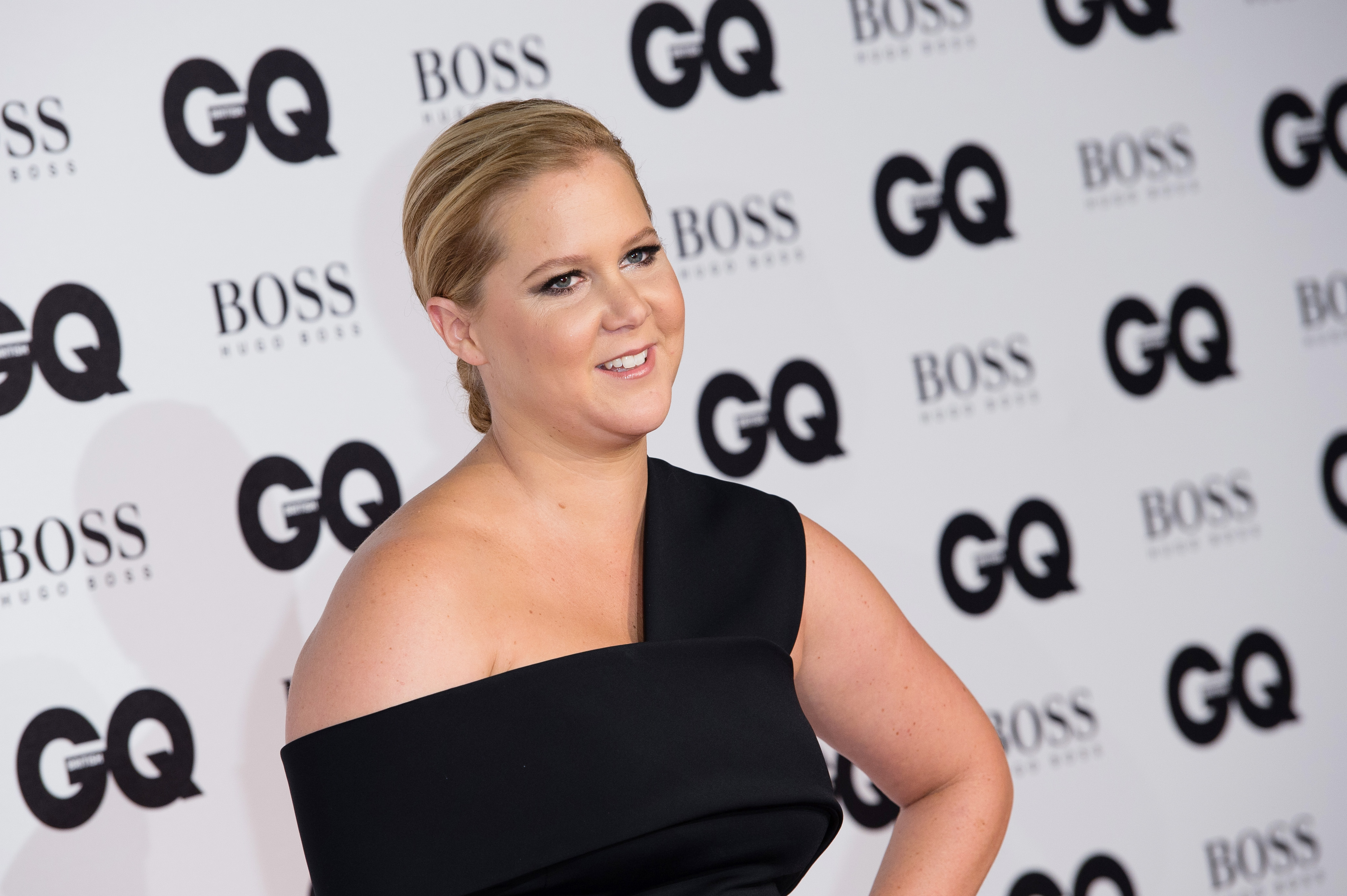 Amy Schumer poses on the red carpet at the GQ Men of the Year Awards in London. She wears a sleek black one-shoulder gown with her hair pulled back in a polished updo.
