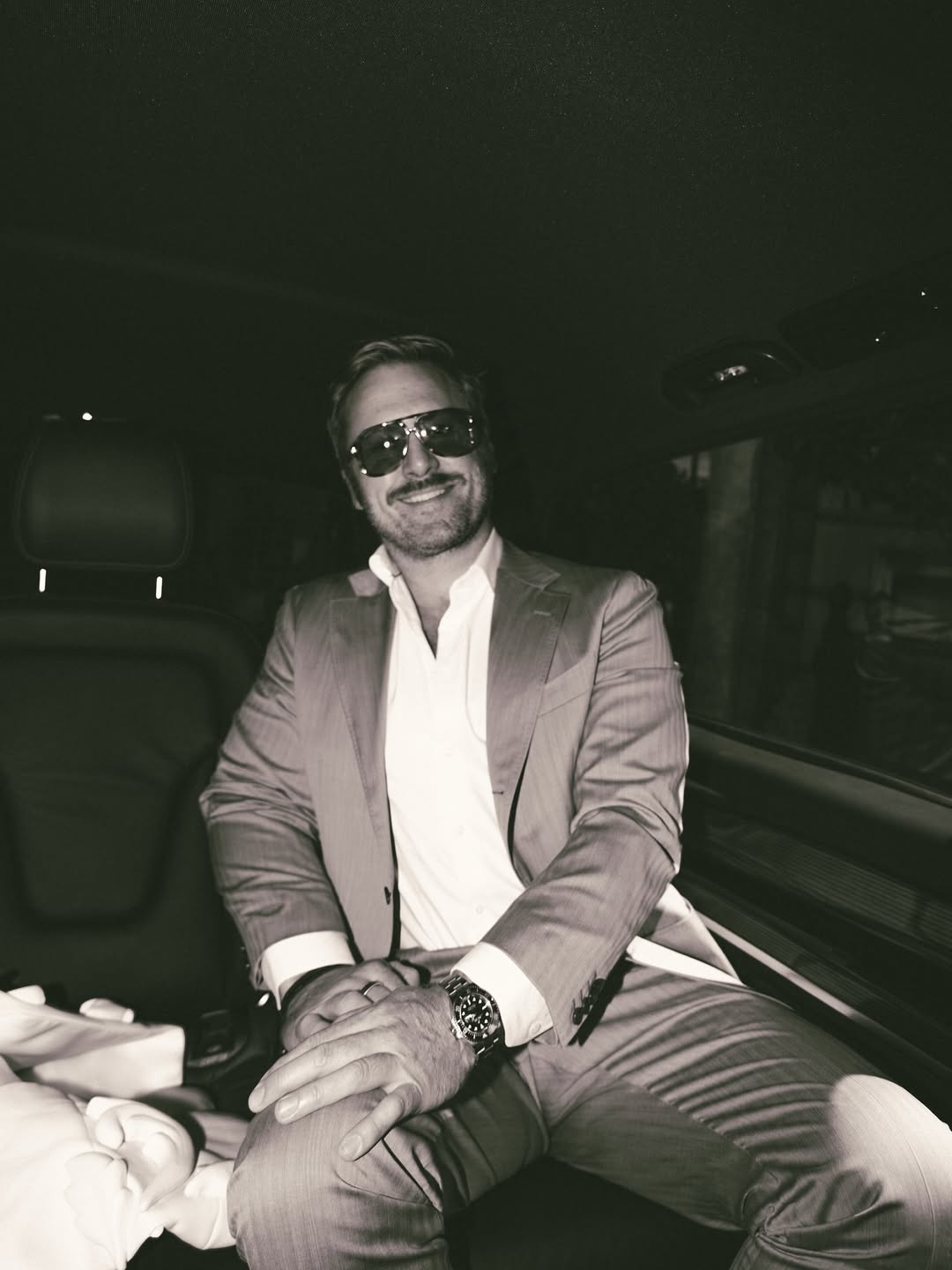Andrew Nixon, Kate Walsh’s fiancé, smiles in the backseat of a car wearing a light suit and dark sunglasses | Source: Instagram/katewalsh
