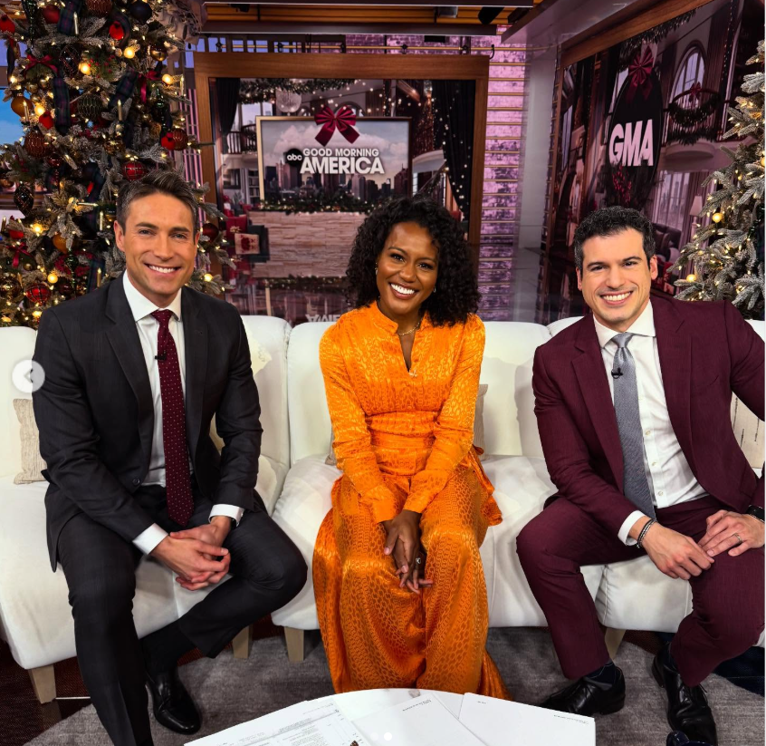 Janai Norman sits center in a vibrant orange dress, smiling warmly between Whit Johnson and Gio Benitez on the "Good Morning America" set. | Source: Instagram/whitjohnsontv