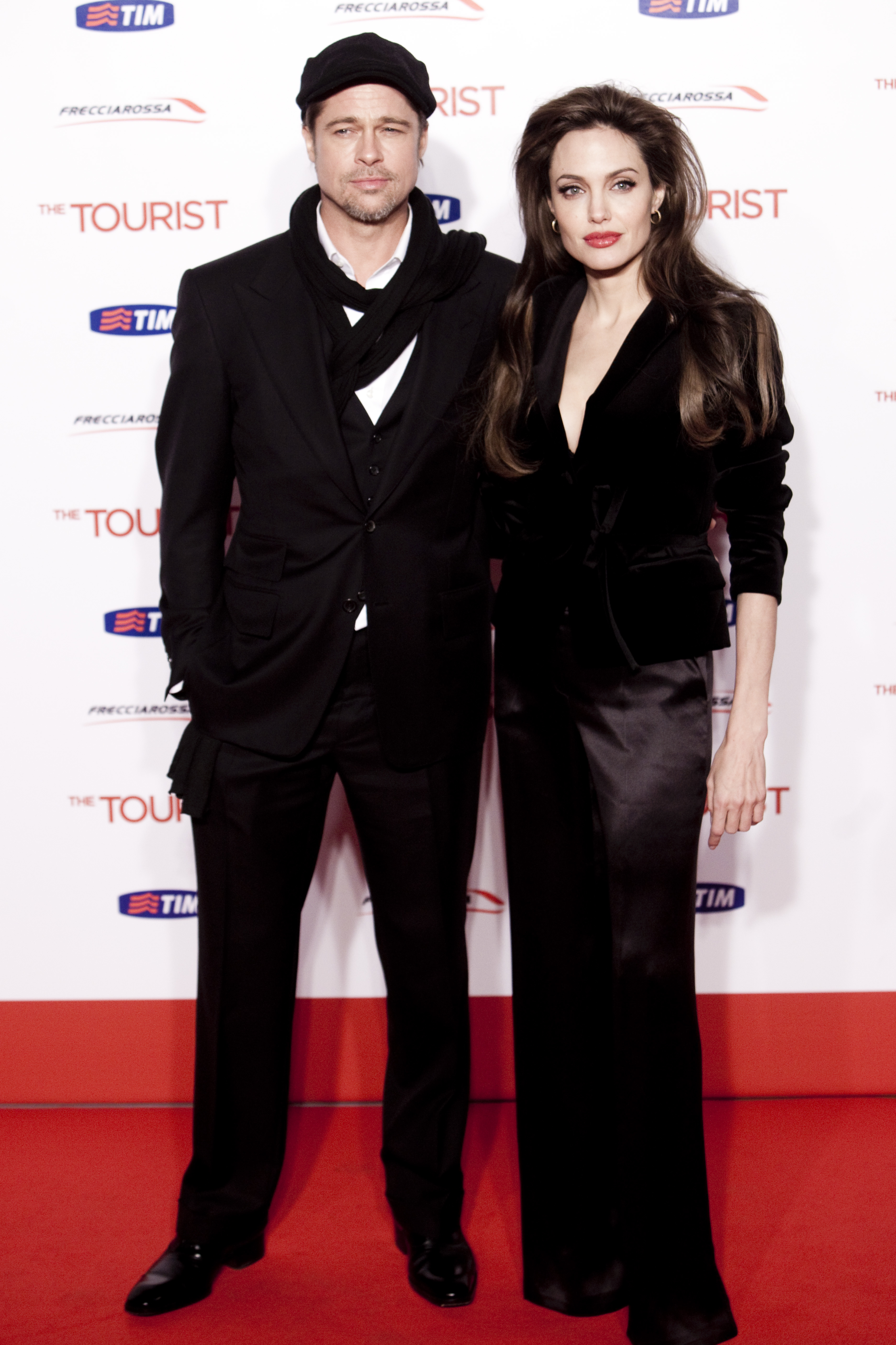 Brad Pitt and Angelina Jolie stand side-by-side at "The Tourist" premiere in Rome, coordinating in elegant dark outfits against the film's white-and-red backdrop.