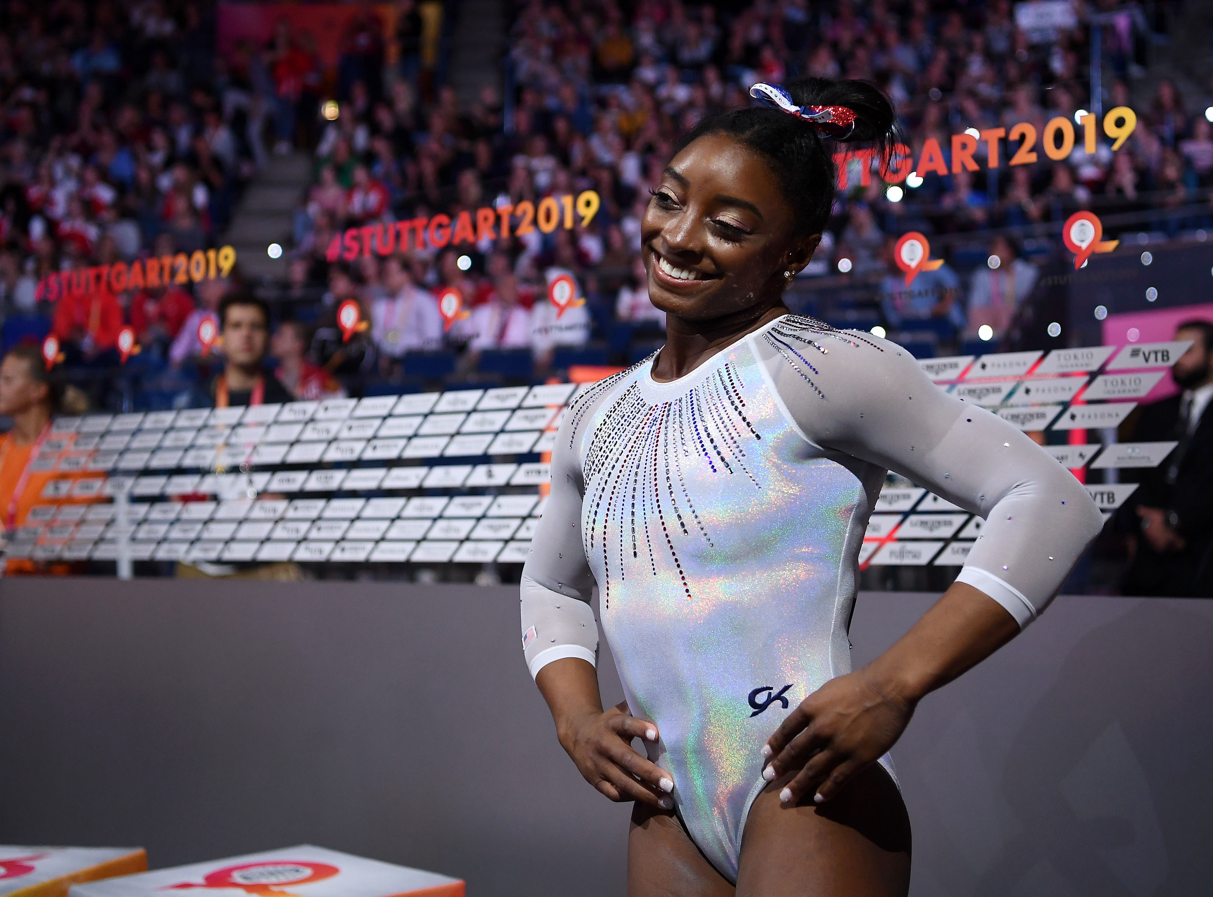 Standing tall with her hands on her hips and a playful smile, Simone Biles commands attention in a dazzling silver leotard during the All-Around Final in Stuttgart on October 10, 2019.