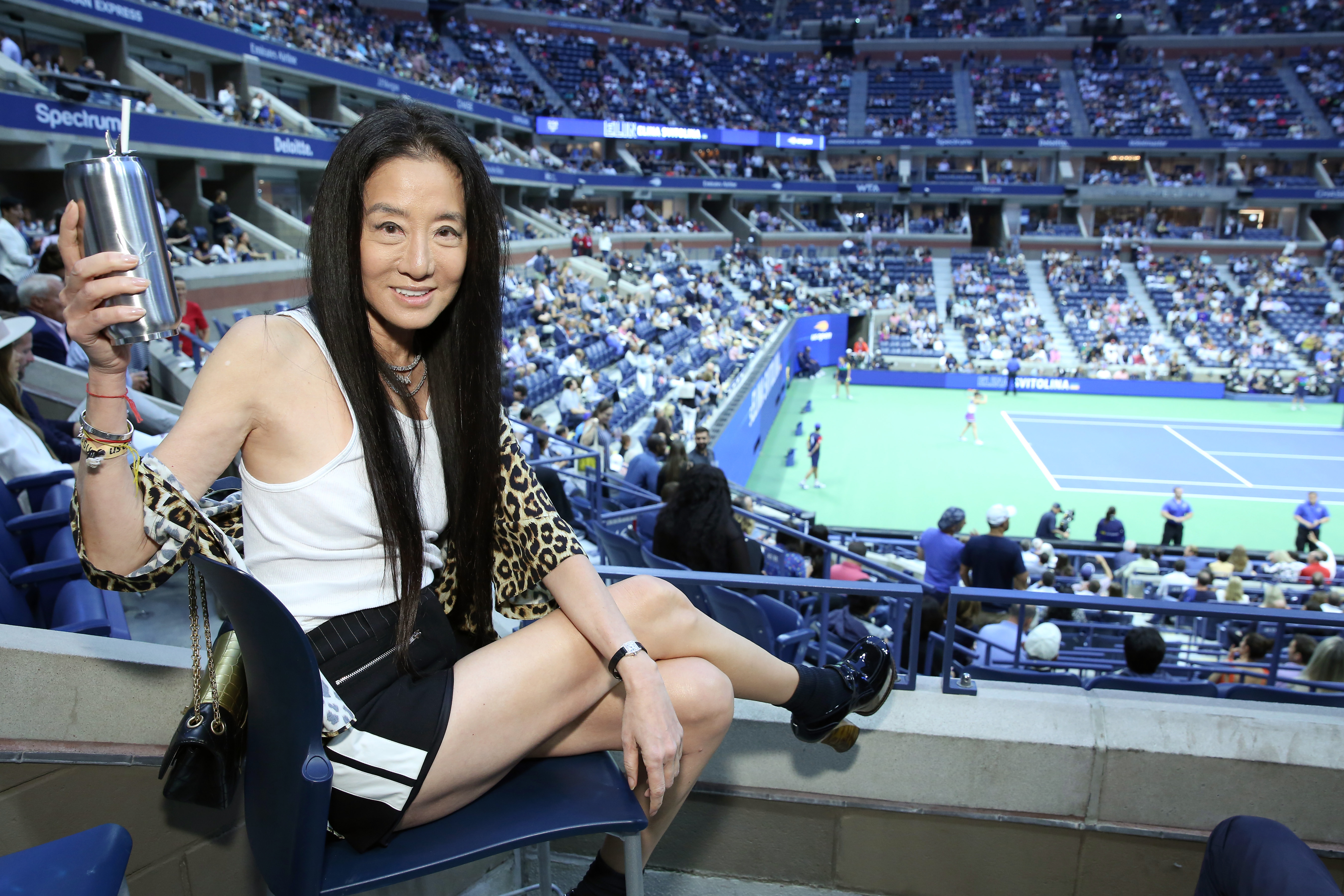 Vera Wang raised a silver tumbler from her stadium seat during the Grey Goose toast to the 2019 US Open at Arthur Ashe Stadium on September 5, 2019, in New York City. Overlooking the tennis court, the designer opted for a sporty yet glamorous look, pairing a simple white tank top and black-and-white athletic shorts with a draped leopard-print layer, patent platform heels, and her signature flowing raven tresses. | Source: Getty Images
