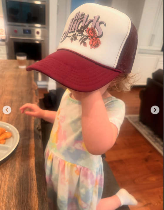 Kaliyah pulls a burgundy-and-white cap over her face while standing beside a kitchen counter. The hat features The Judds' name and a rose design, connecting the family photograph to Wynonna's musical history. | Source: Instagram/wynonnajudd