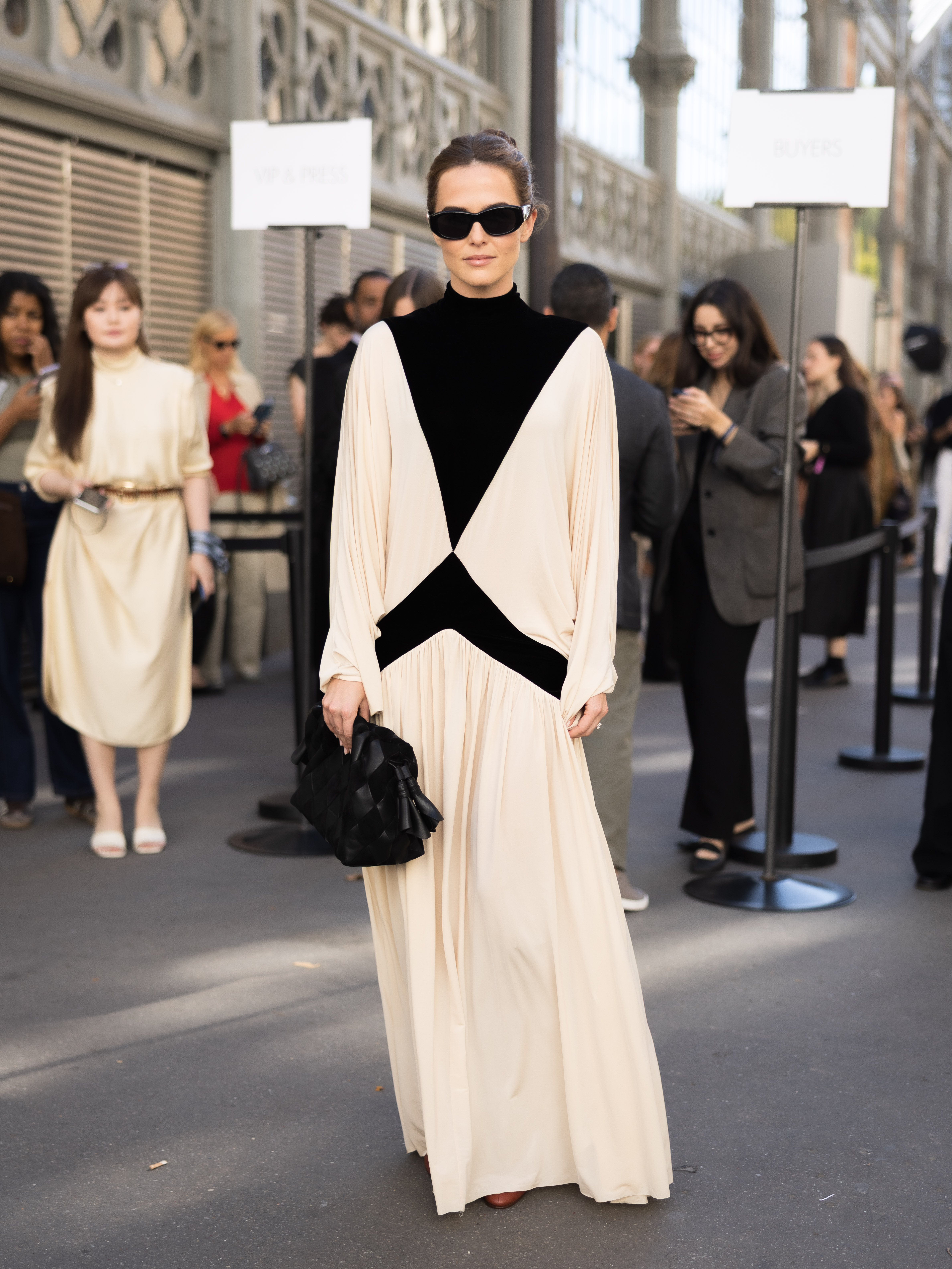 Bold black panels cut across Zoey Deutch's cream dress, creating a strong geometric contrast from the neckline to the waist. She keeps the rest of the look simple with dark sunglasses and a black handbag.