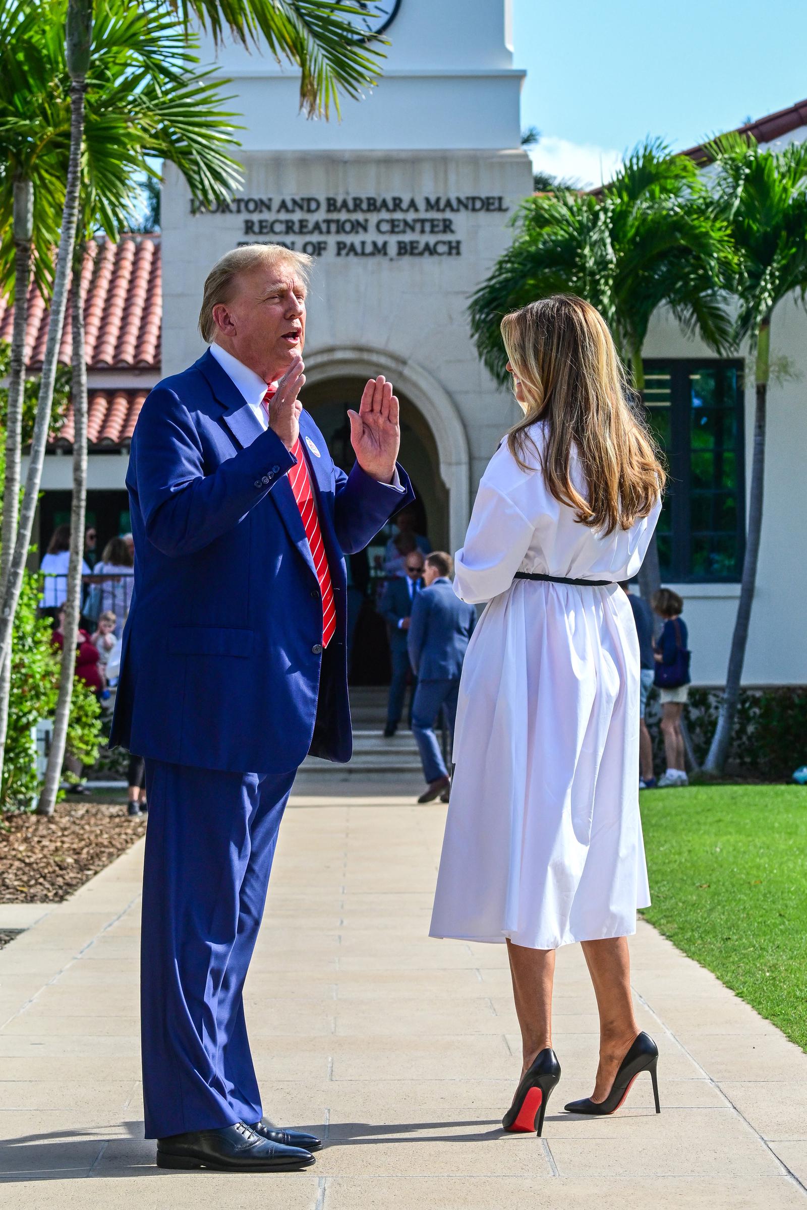 Former First Lady Melania Trump talks with Donald Trump as they arrive to vote in Florida's presidential primary election at the Morton and Barbara Mandel Recreation Center in Palm Beach, Florida, on March 19, 2024, wearing a crisp white collared midi dress cinched at the waist with a slim black belt and accessorized with Christian Louboutin black patent leather pointed-toe pumps that display sky-high stiletto heels and vibrant red lacquered soles.