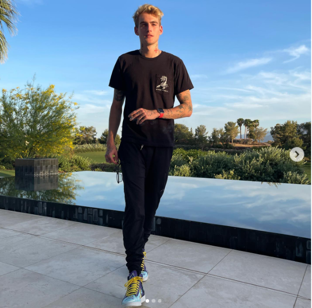 In an outdoor snapshot shared on April 11, 2021, Presley Gerber walked alongside an infinity pool against a backdrop of lush greenery, dressed in an all-black casual look featuring a graphic pocket T-shirt, black sweatpants, and vibrant colorful sneakers. | Source: Instagram/presleygerber