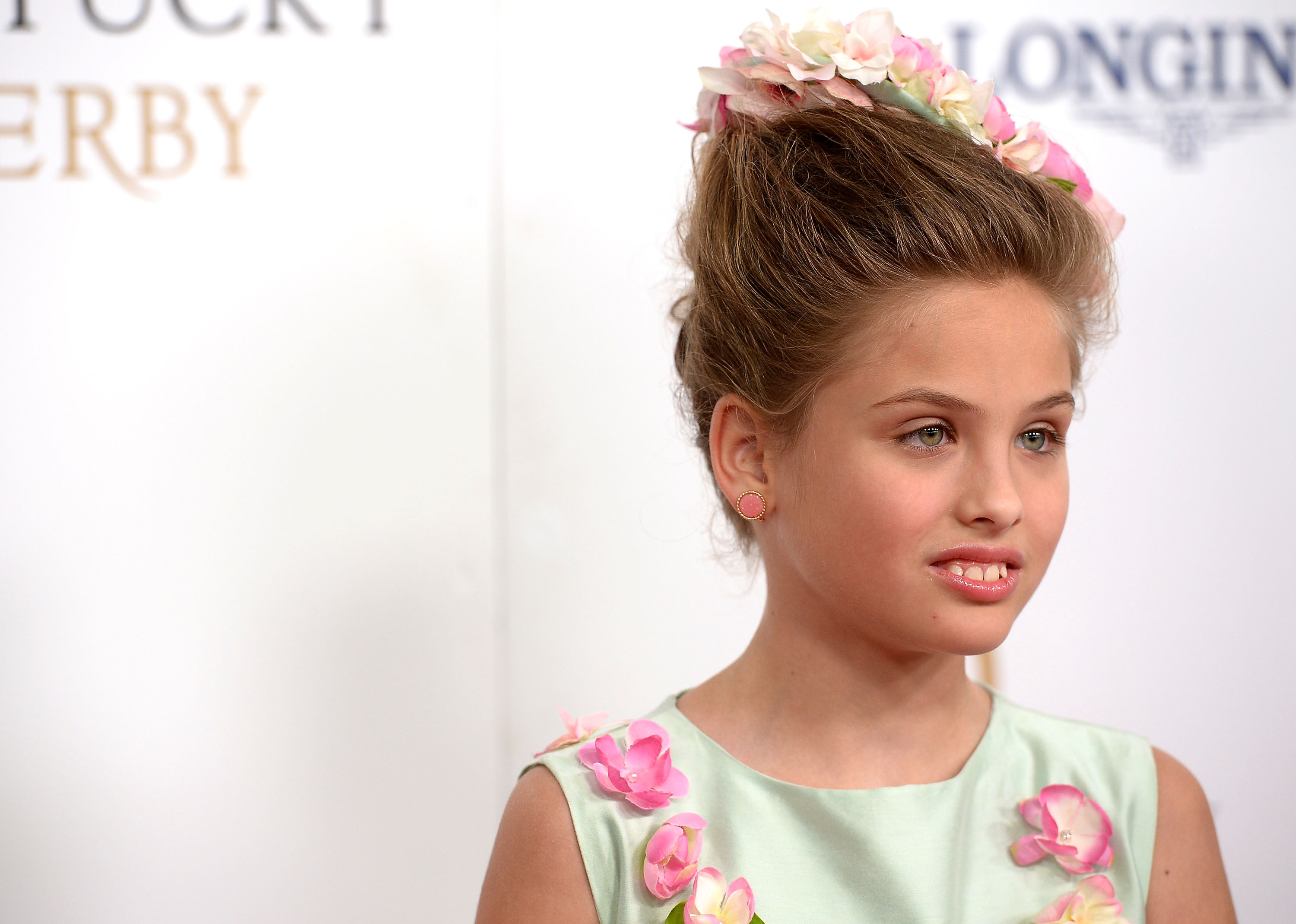 Swept up into a sophisticated updo and crowned with a delicate halo of pastel pink and cream blossoms, 9-year-old Dannielynn Birkhead exuded effortless elegance at the 142nd Kentucky Derby at Churchill Downs on May 7, 2016. A mint-green dress featuring charming floral appliqués along the neckline and matching pink stud earrings completed her polished attire, highlighting her graceful emergence into a poised young pre-teen with a distinct, refined style of her own.