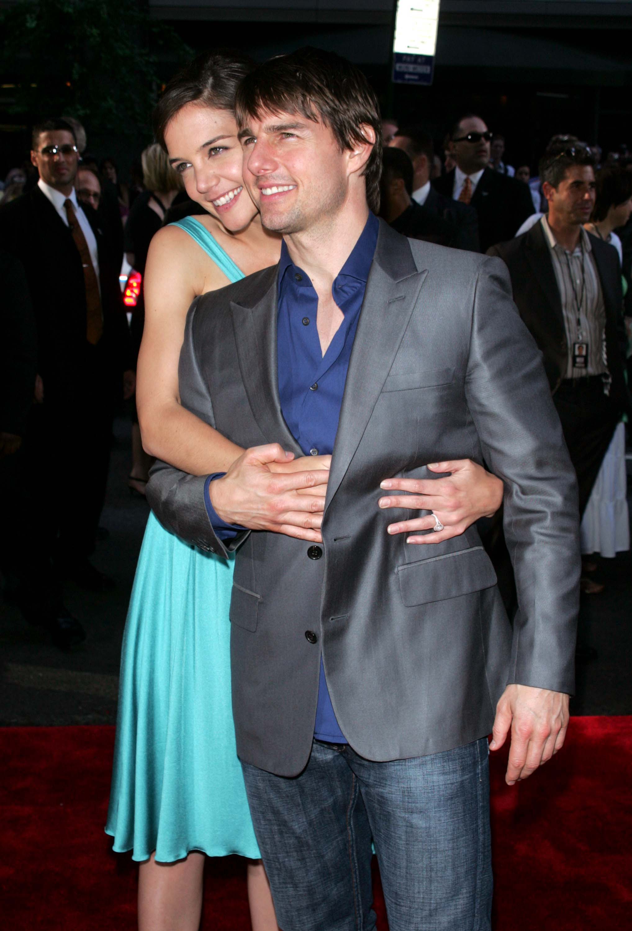 Katie Holmes beamed as she lovingly embraced Tom Cruise from behind, her turquoise dress adding a pop of color against his sharp gray suit. The then-couple radiated joy and closeness, drawing attention with their coordinated charm and warmth.