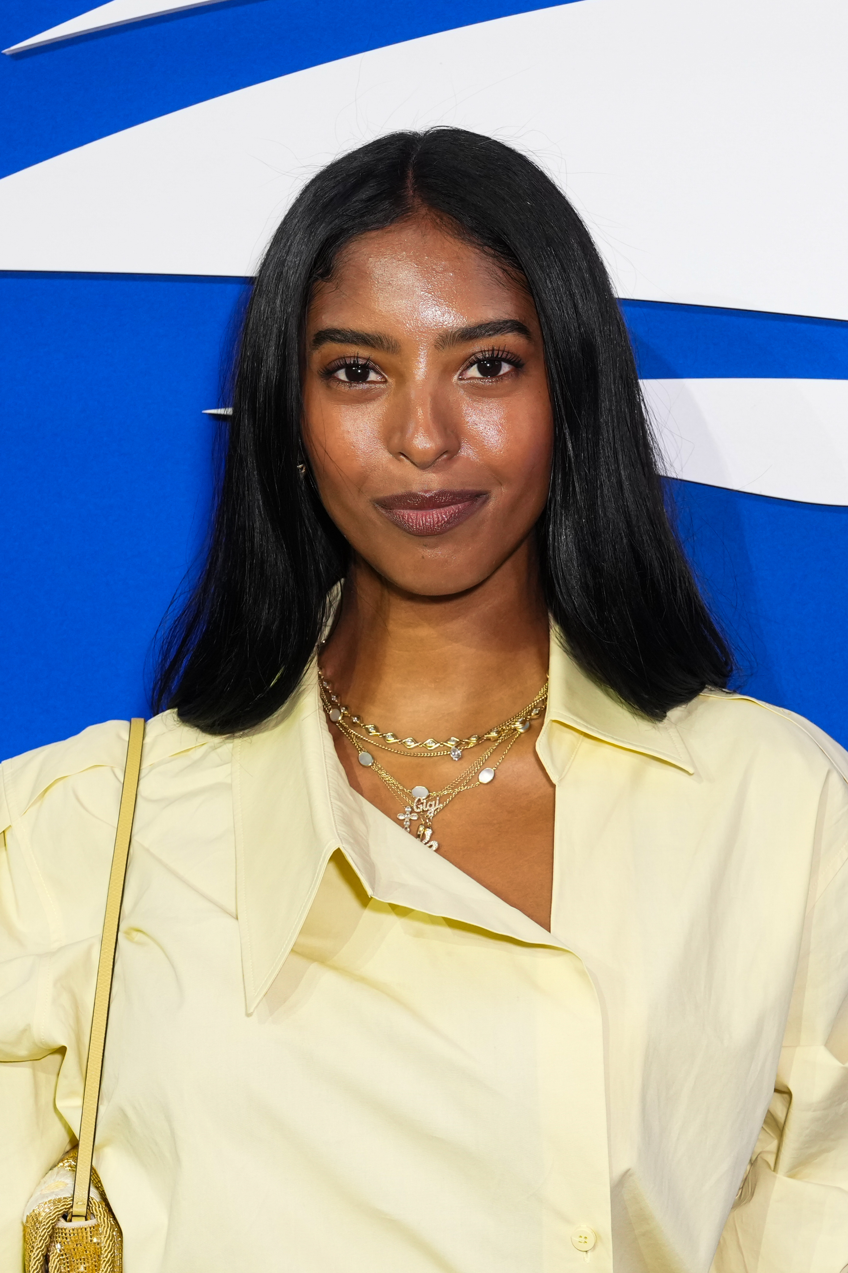 Natalia Bryant poses at the 2026 US Open in New York, wearing a pale-yellow ensemble with a statement collar and layered necklaces as she embraces a polished, fashion-forward look.