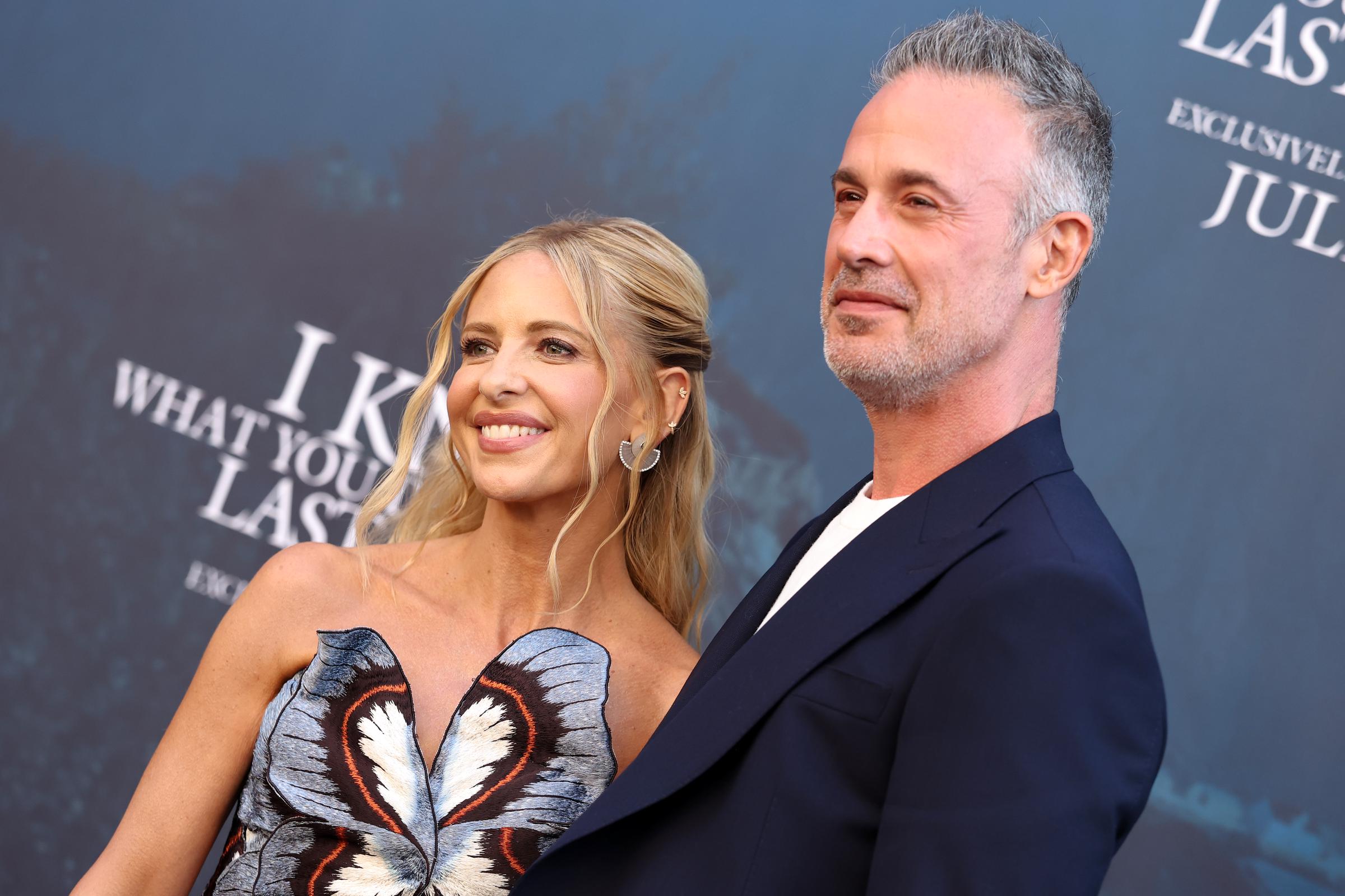 Gellar and Prinze Jr. pose side by side, both smiling as they look slightly off-camera. She leans slightly towards her husband, while he stands straight with a relaxed, confident expression.