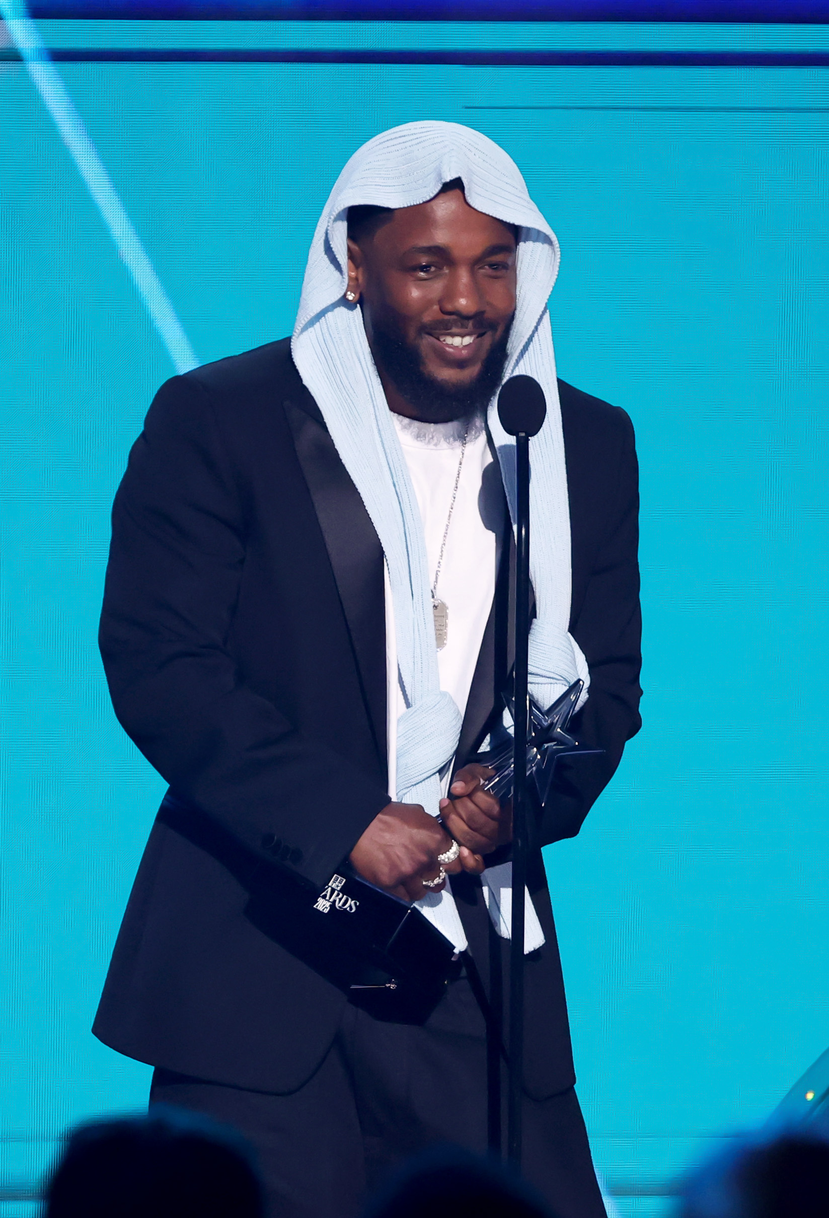 Kendrick Lamar beams onstage while accepting Album of the Year for "GNX" at the 2025 BET Awards, hosted at the Peacock Theater. The rapper's striking look and genuine smile lit up the room as fans erupted in applause.