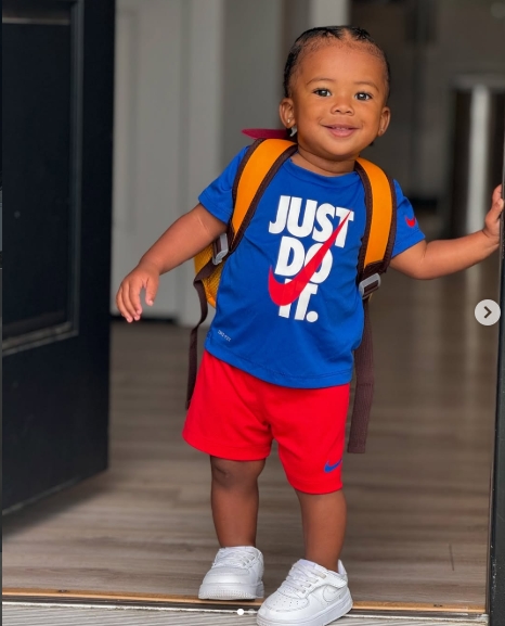 A smiling Tyreek Jr. stands in a doorway with a backpack over his shoulders, dressed in a bright blue Nike "Just Do It" T-shirt, red shorts, and white sneakers. The casual snapshot captured Tyreek Hill and Camille Valmon's young son on the move more than a year after his birth. The image appeared in a post dated July 24, 2024. | Source: Instagram/tyreekhilljr_