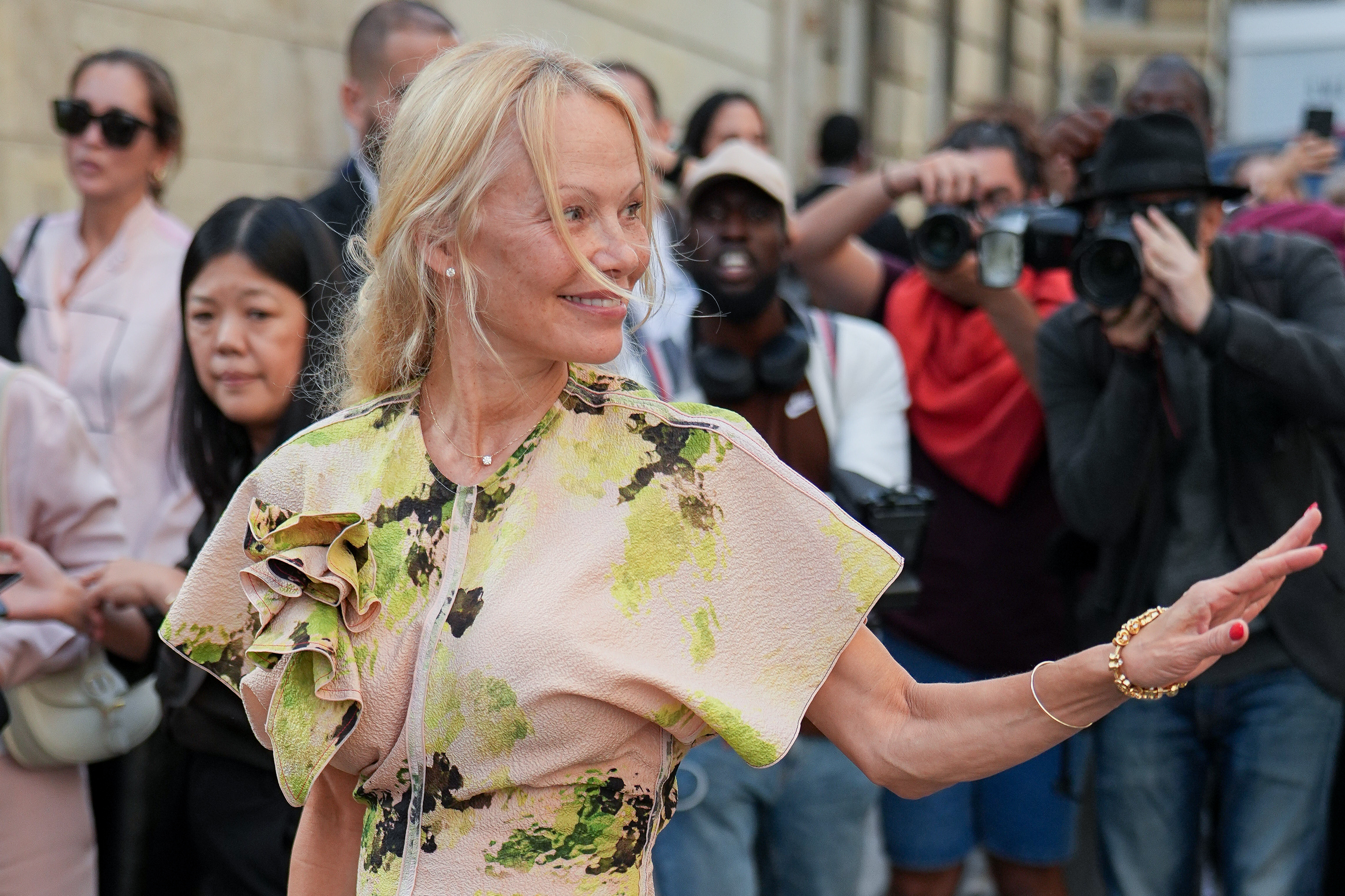 Pamela Anderson, makeup-free with her hair loosely tied back, wears a pale pink and green floral dress with ruffled sleeves at the Victoria Beckham show during Paris Fashion Week, on September 29, 2023, in France.