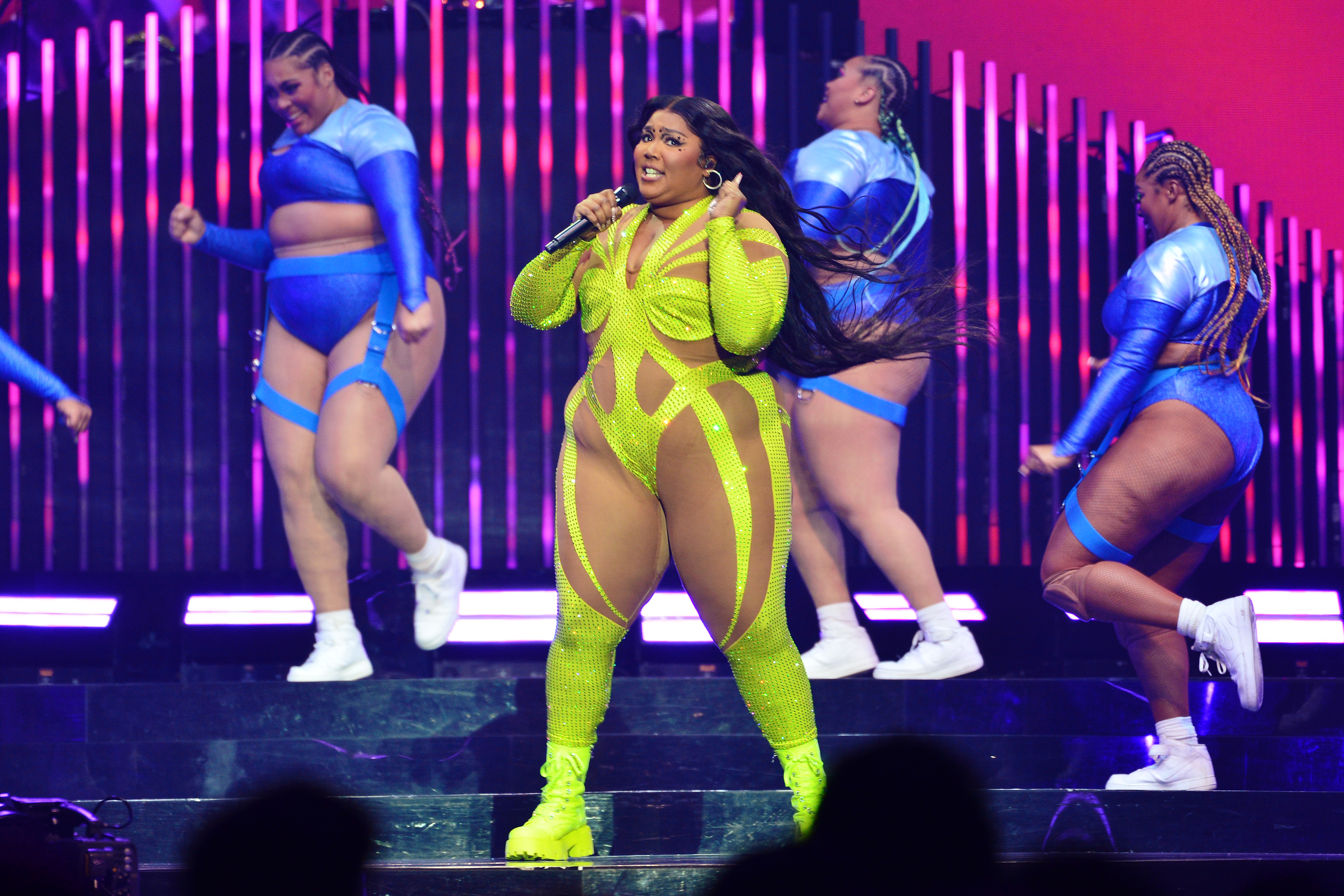 During her March 2023 performance at The O2 in London, Lizzo wore a neon green crystal-studded bodysuit with sheer nude paneling that clung tightly to her visibly larger frame. The bold cutouts and skin-tight fit highlighted her fuller arms, thick thighs, and prominent midsection.