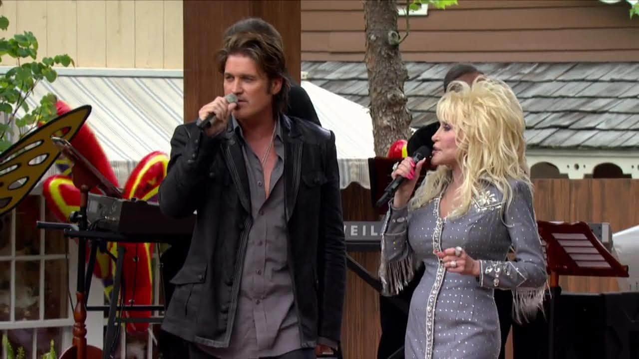 Performing live together: Dolly Parton, elegant in a grey sequined dress, and Billy Ray Cyrus sing duets on stage during an outdoor concert appearance. | Source: Facebook/BillyRayCyrus