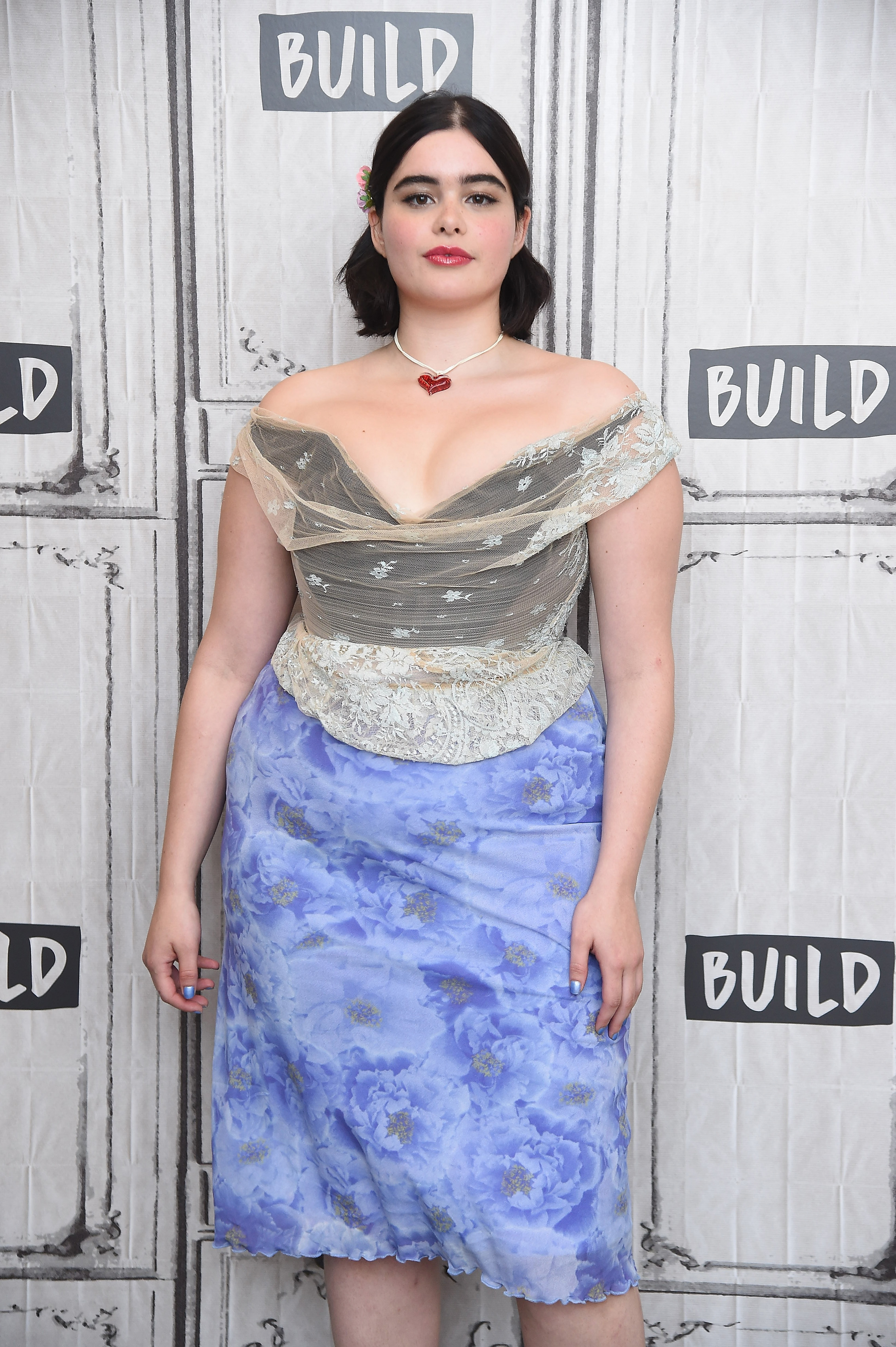 Ferreira is seen visiting the Build Series studio in New York City on July 25, 2019, where she discussed the HBO series "Euphoria." She wears an off-the-shoulder lace corset top with a sheer overlay paired with a periwinkle blue floral skirt. Her look is completed with a red heart pendant necklace, soft makeup, and shoulder-length hair adorned with small floral clips.