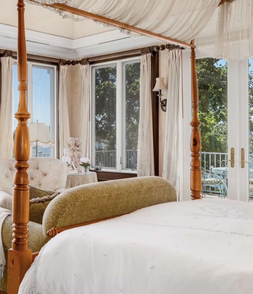One of Cedar Cliff's elegant bedrooms features a four-poster canopy bed, soft cream furnishings, and French doors opening onto a private terrace — combining traditional luxury with beautiful views of the grounds. | Source: Instagram/@robbreport