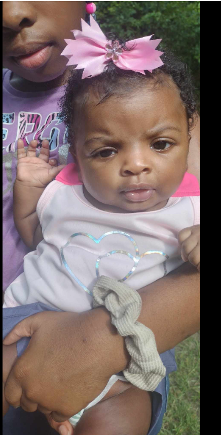 A close-up of two of Shamar Elkins’s children shows a baby with a pink bow resting in the arms of an older child just out of frame. | Source: Facebook/Shaneiqua Elkins