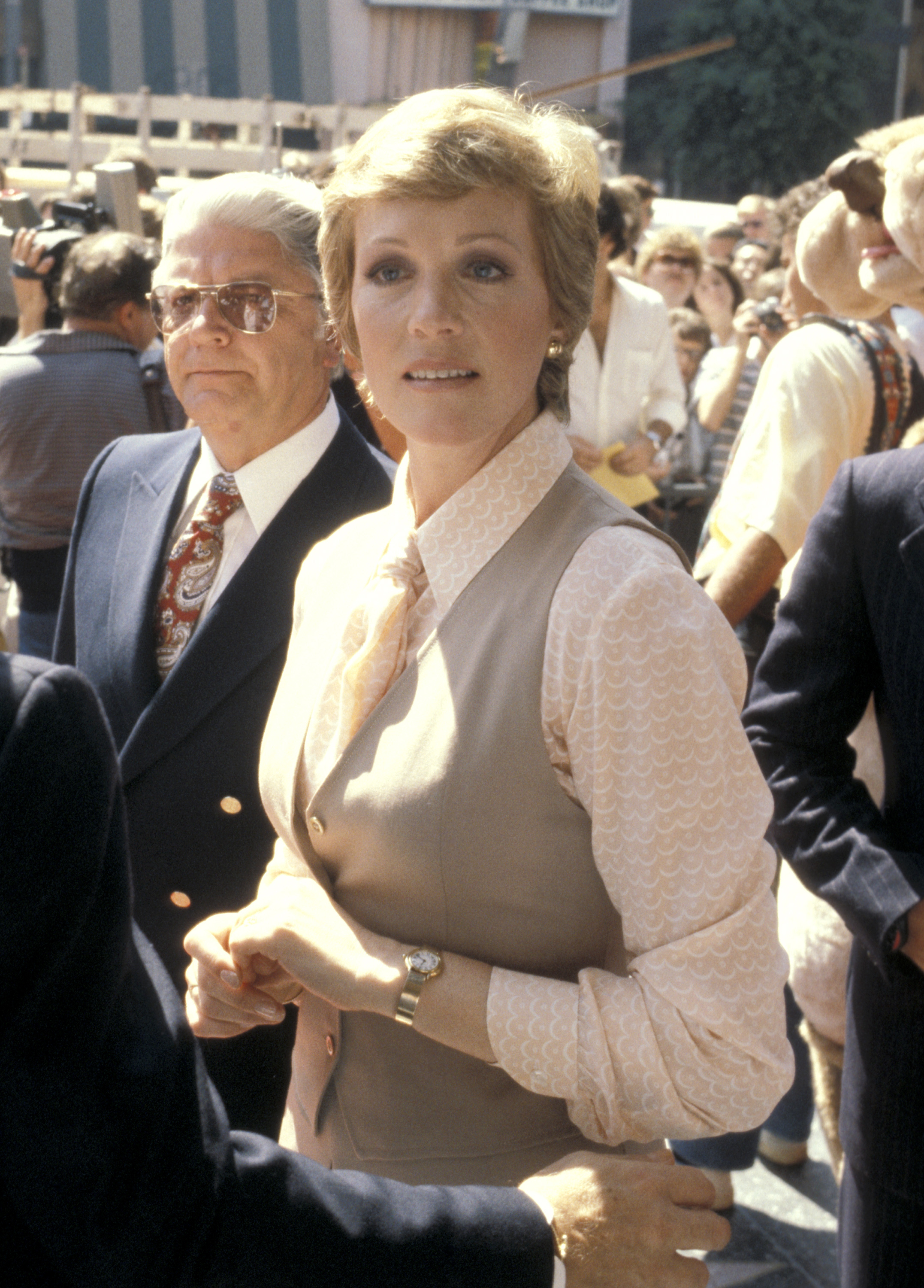 Julie Andrews attends her Hollywood Walk of Fame star ceremony at 6901 Hollywood Boulevard in Los Angeles on October 5, 1979. Surrounded by crowds and photographers, the celebrated actress radiates polished late-’70s elegance in a beige tailored vest layered over a patterned silk button-down blouse with an ascot tie collar, accessorized with pearl earrings and a gold wristwatch.
