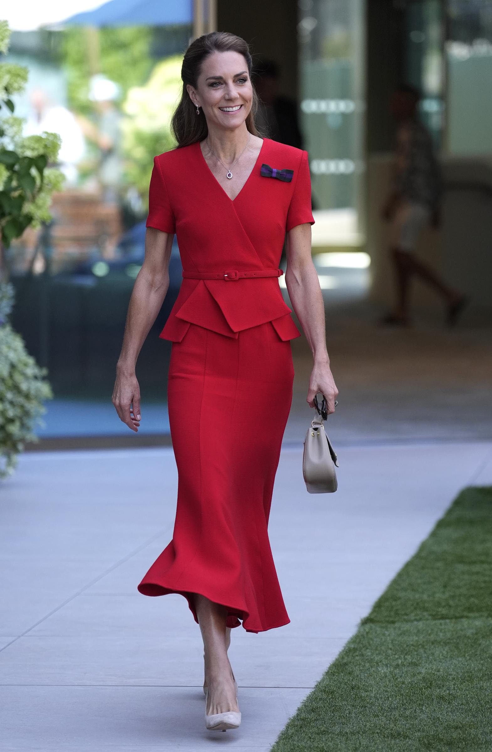 The fitted red dress featured a wrapped bodice, a slim belt, and a peplum waist that created a more structured silhouette than her first Wimbledon look. Nude heels and a neutral handbag kept the focus on the vivid color. | Source: Getty Images