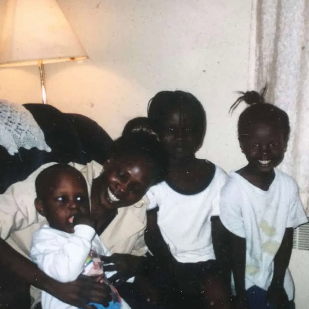 Anok Yai as a toddler, standing on a table in a white dress, with family in the background | Source: Instagram/anokyai