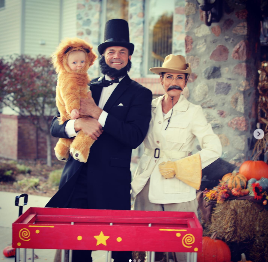At the center, Bryon Noem, dressed as Abraham Lincoln, holds a baby in a fuzzy lion costume, while Kristi Noem, styled as a vintage explorer with a safari hat and curled mustache, adds a playful twist beside him. | Source: Instagram/sdbryonnoem