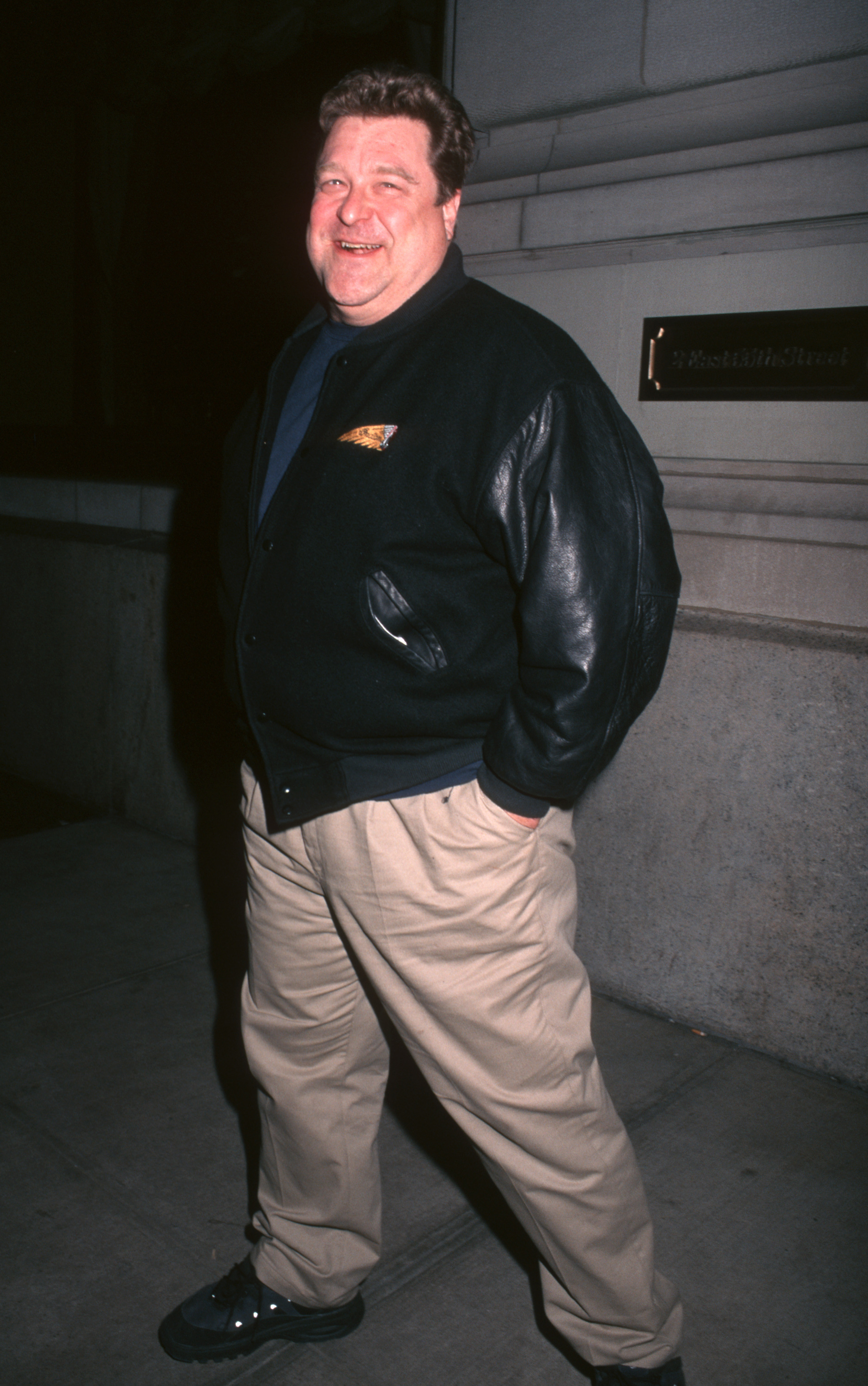 Goodman smiled for photographers outside the St. Regis Hotel in New York City, wearing a dark jacket and light-colored pants. With his hands tucked into his pockets, the casual image offers another clear view of his earlier physique before his later transformation.