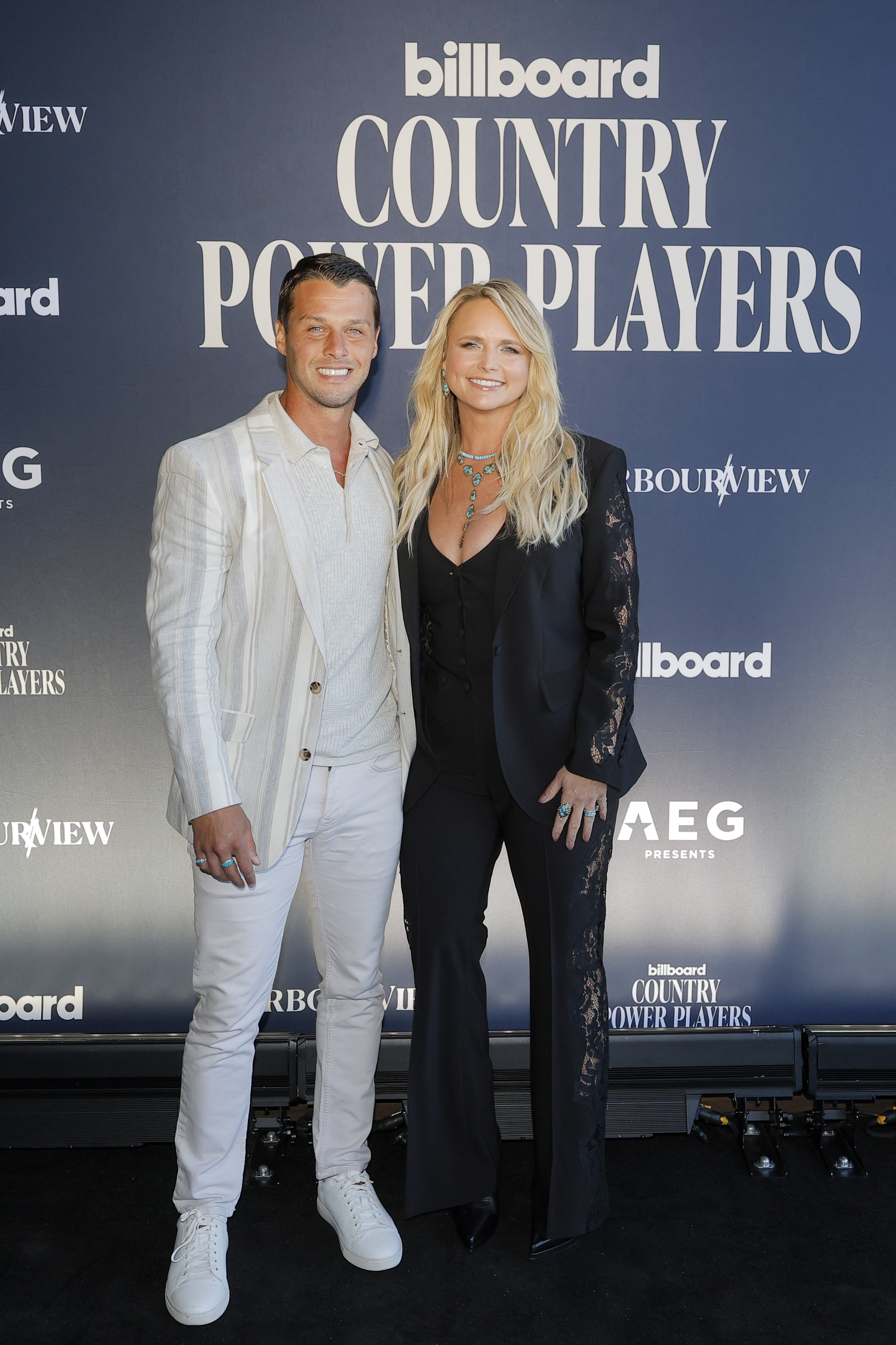 Brendan McLoughlin and Miranda Lambert made a stylish entrance at the Billboard Country Power Players 2026 event at Category 10 on June 3, 2026, in Nashville, Tennessee. Miranda rocked a chic black pantsuit accented with sheer lace panels along the sleeves and trousers, pairing the tailored look with turquoise jewelry. Brendan complemented her sharp aesthetic in a striped cream blazer, casual henley, crisp white jeans, and sneakers. | Source: Getty Images