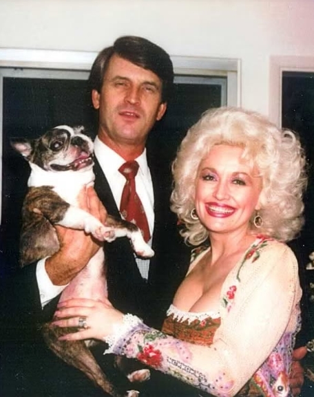 Dean held a dog while Parton beamed beside him in this candid photograph. The image captured the couple in a more relaxed setting than the public events associated with her career. Their easygoing appearance offered a glimpse into the private life they shared beyond Parton's performances and celebrity commitments. The singer later explained that she and Dean preferred simple activities together and had little interest in the party scene. | Source: Facebook/One Country