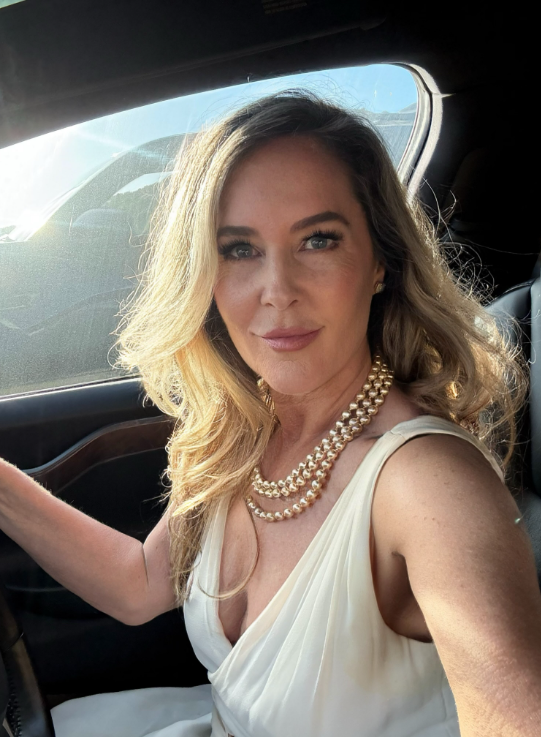 Erin Murphy sits in the driver's seat wearing a white dress and layered gold necklaces as sunlight falls across her hair. The close-up selfie is the photo that sparked fresh comments about how different she looks today. | Source: Instagram/erinmurphybewitched