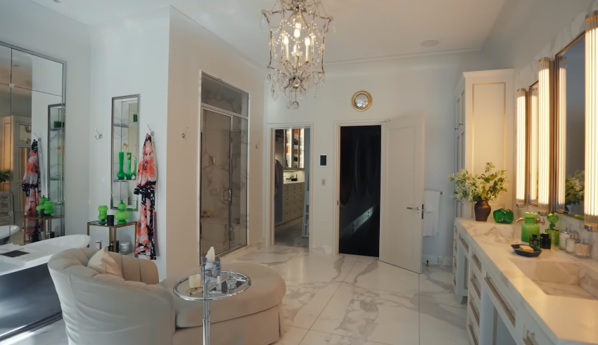 The lighted mirrors and marble floors make the room feel deliberately cinematic. It is pristine, polished, and very much built around a fantasy. | Source: YouTube/Architectural Digest
