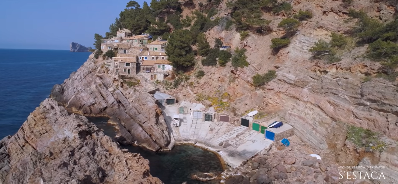 Several buildings sit directly above the rocky shoreline, with steps leading down toward the water. The dramatic setting shows how closely this part of the property meets the Mediterranean. | Source: YouTube/billionsluxuryportal