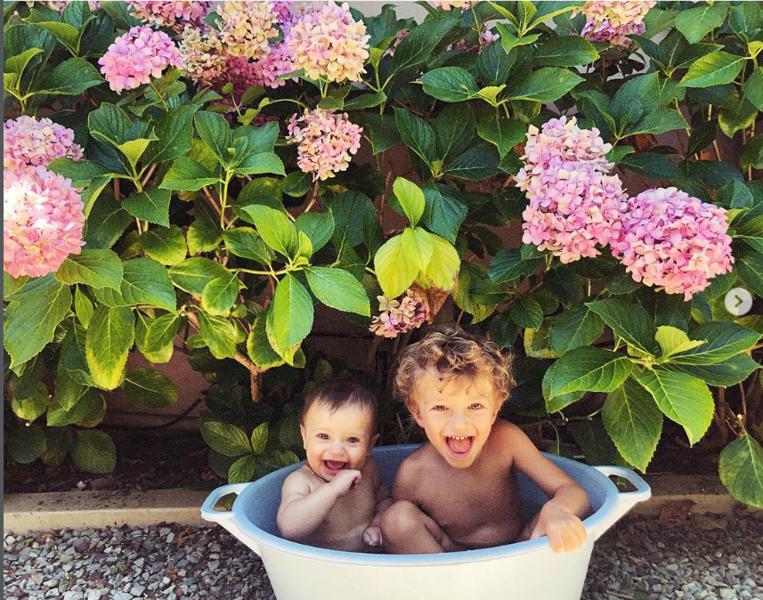 Candice Swanepoel's two sons, Anacan and Ariel, share a joyful moment together in a tub outdoors, surrounded by lush greenery and pink flowers. The playful photo offers a sweet glimpse of the brothers enjoying time together away from their mother's busy modeling career. | Source: Instagram/candiceswanepoel