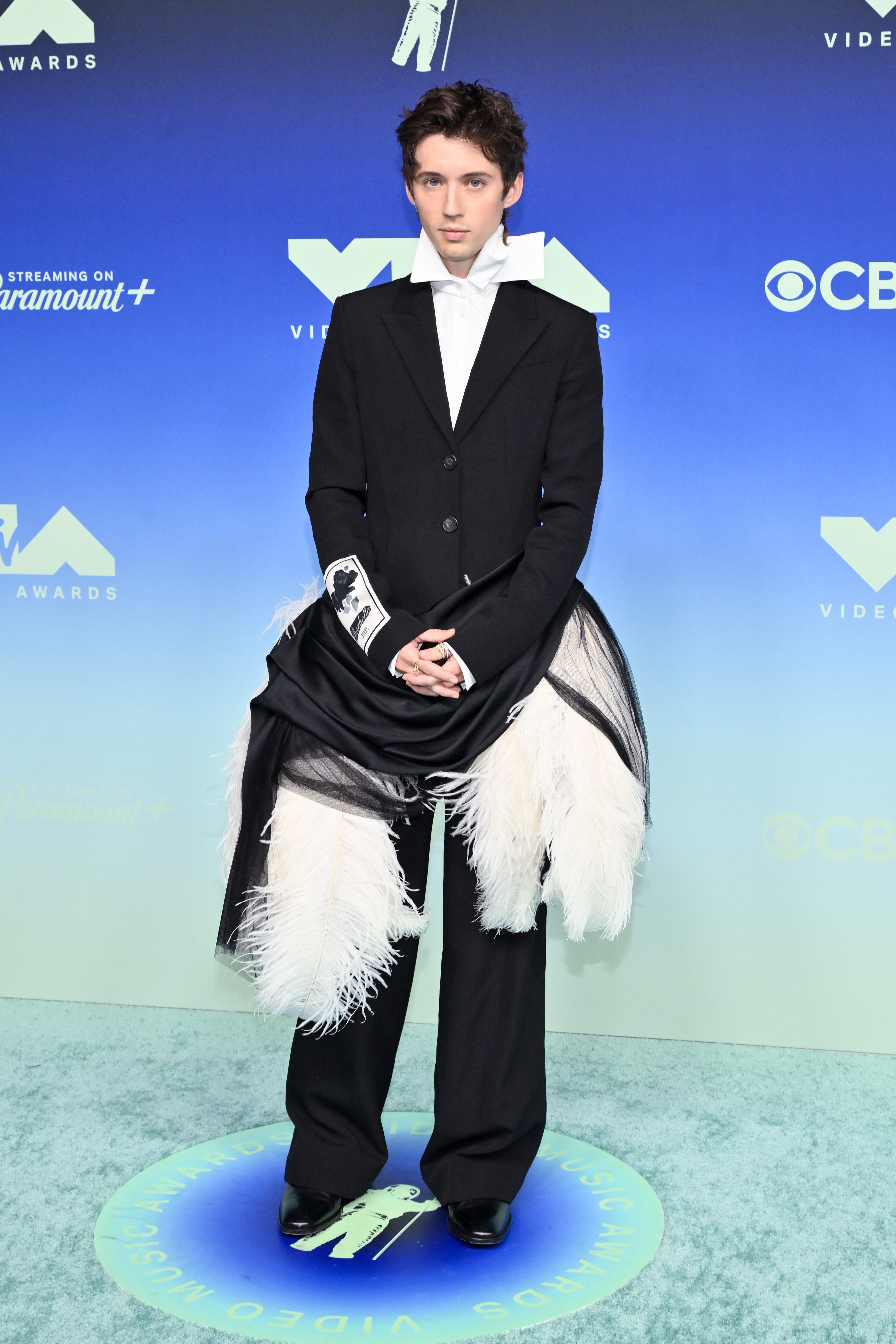 Sivan disrupted a traditional black suit with an oversized white bow and large feathered panels around his thighs. Draped black fabric at the waist added another layer between the fitted jacket and loose trousers. | Source: Getty Images