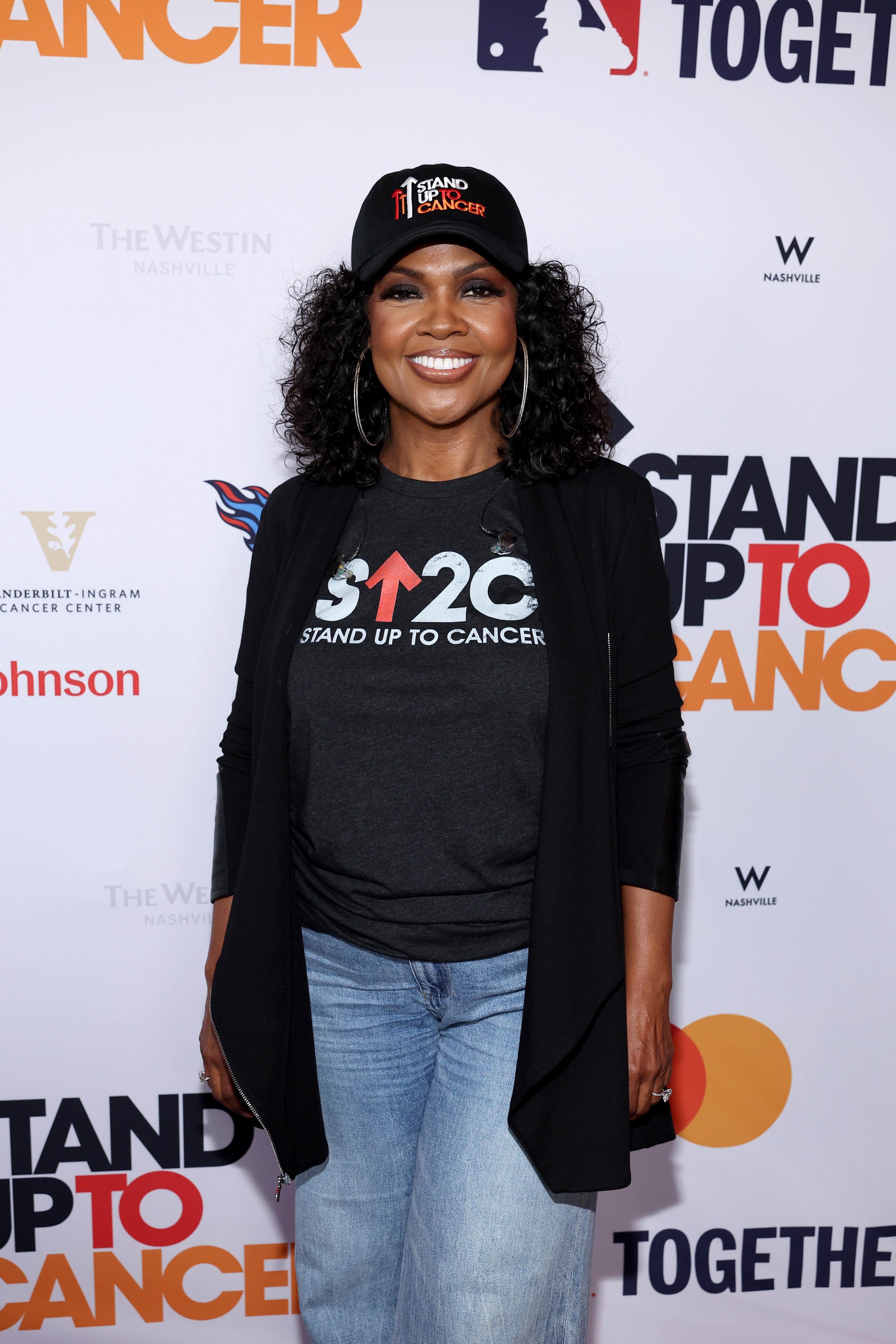 CeCe Winans smiles while attending the Stand Up To Cancer Telecast 2025 in Nashville, Tennessee, on August 9, 2025, wearing a black cap, jeans, and a graphic T-shirt.