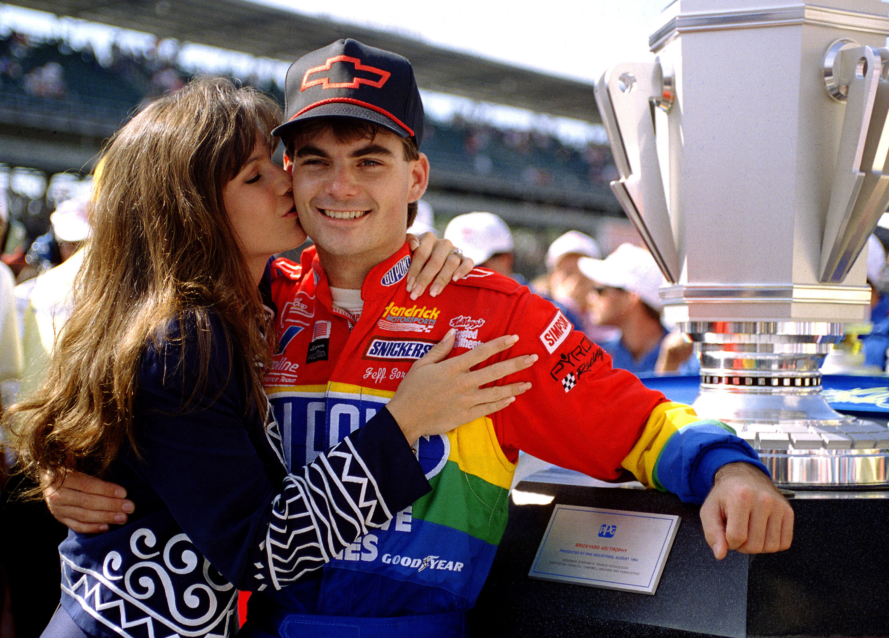 Brooke Sealey planted a congratulatory kiss on fiance Jeff Gordon after he won the inaugural Brickyard 400 at Indianapolis Motor Speedway on August 6, 1994. Gordon posed beside the trophy following his landmark victory, which came during the same year the couple became engaged and later married.