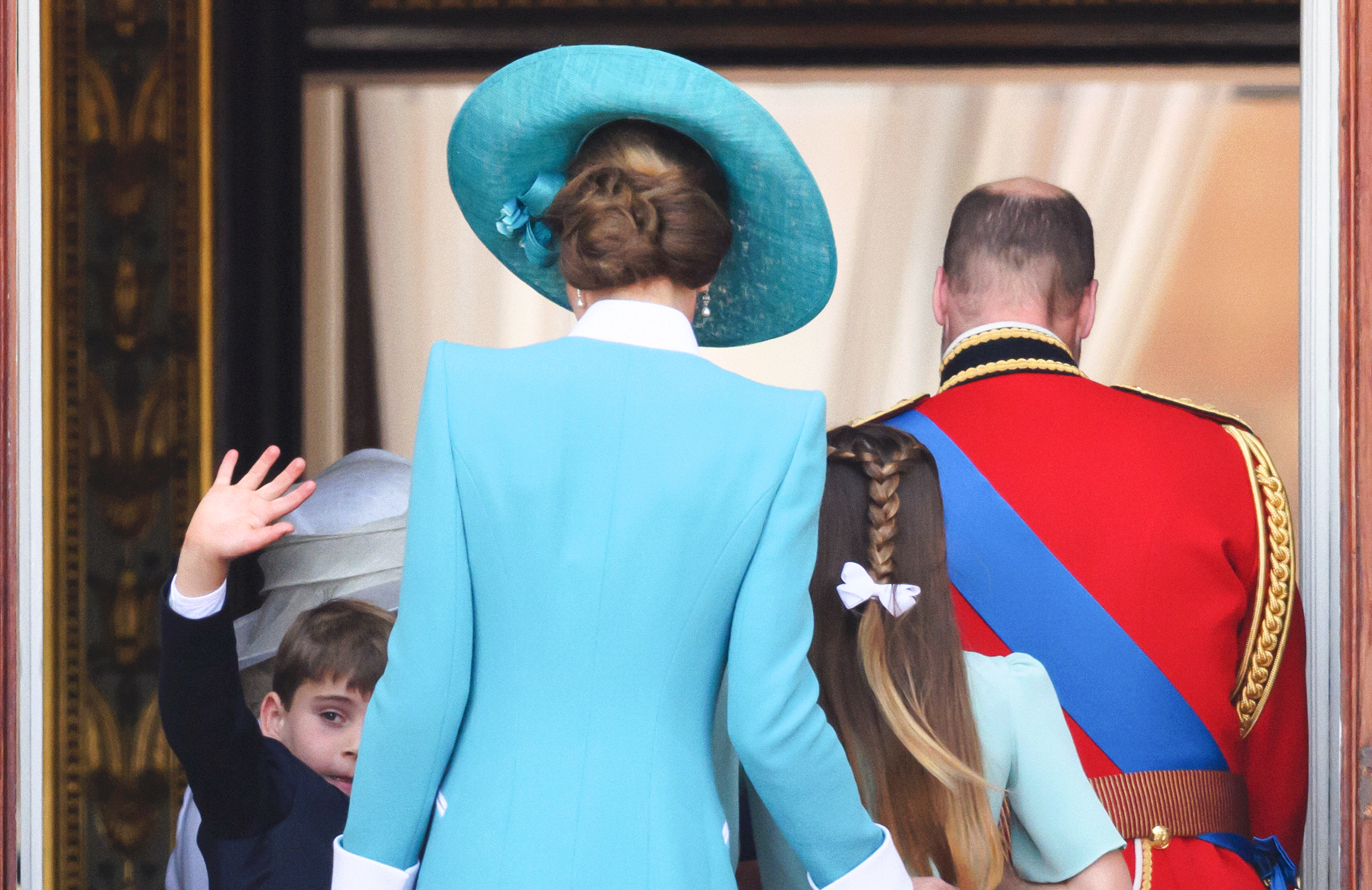 Captured from behind, Prince William, Princess Catherine, and their children—Prince George, Princess Charlotte, and Prince Louis—are seen attending the 2025 Trooping the Colour. Their silhouettes framed by formal attire and regal posture, symbolizing unity and the enduring legacy of the royal line.