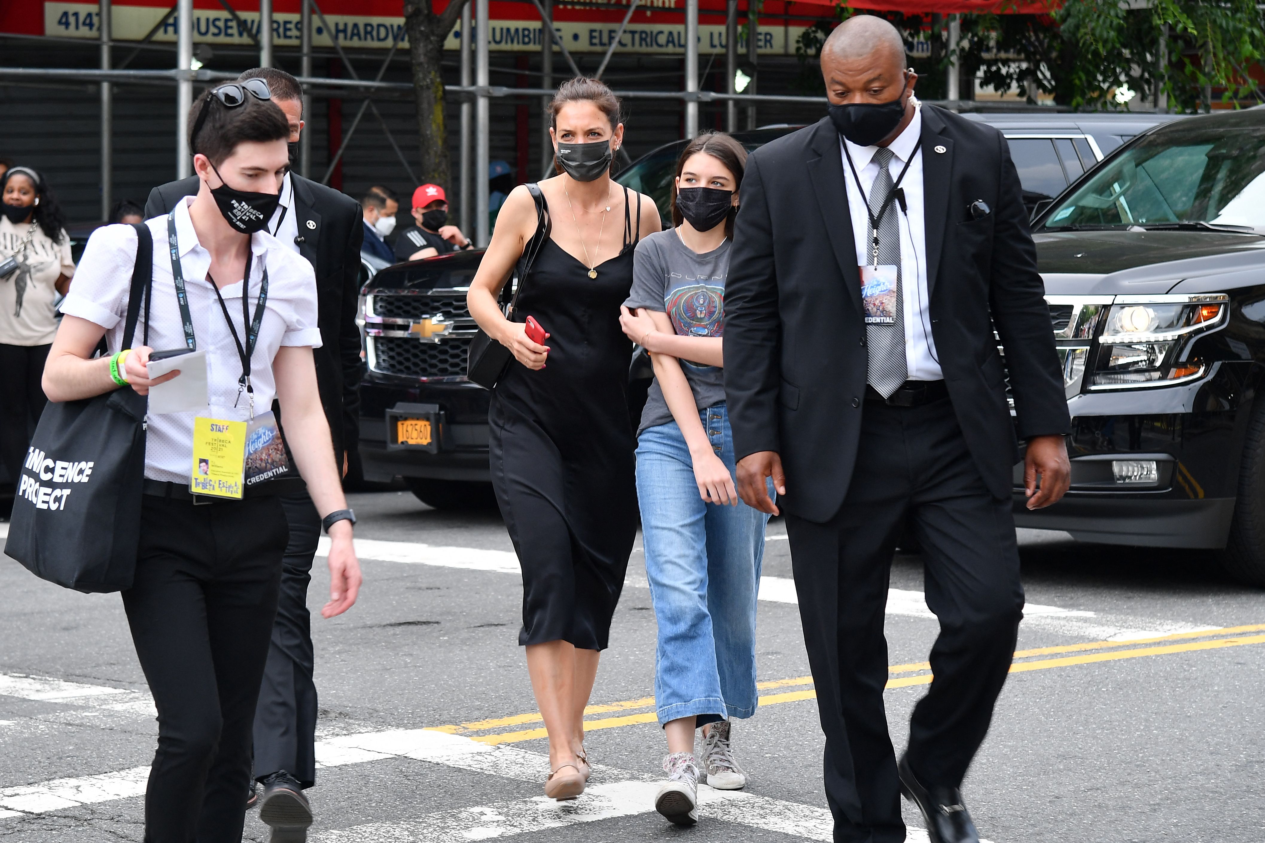 Suri Cruise and her mother, Katie Holmes, are seen crossing a busy street, both wearing black face masks. Flanked by security, the pair move with quiet purpose through the city. The added presence of guards underscores their high-profile status, even during routine outings.