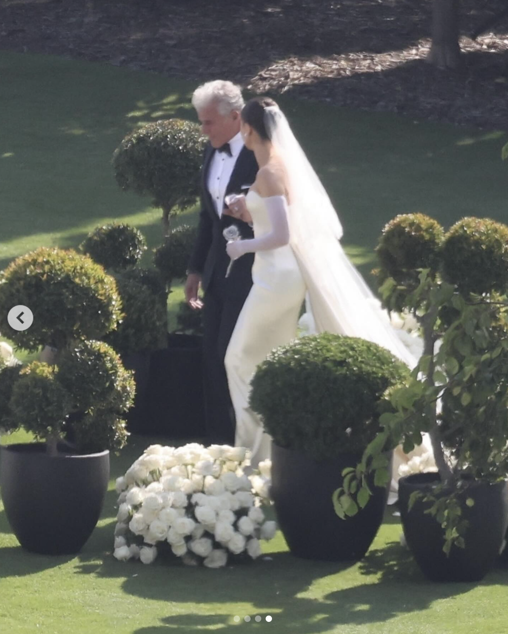 Hailee Steinfeld walks across the lawn in her wedding gown, holding a bouquet, as she's escorted toward the ceremony | Source: Instagram/justjared