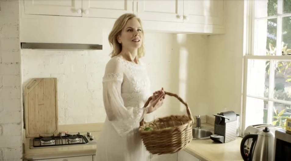 Bathed in sunlight from a large paned window, the farmhouse kitchen features simple cream cabinetry, a stone countertop, and a cozy blend of charm and utility. From a video dated July 20, 2015. | Source: YouTube/Vogue