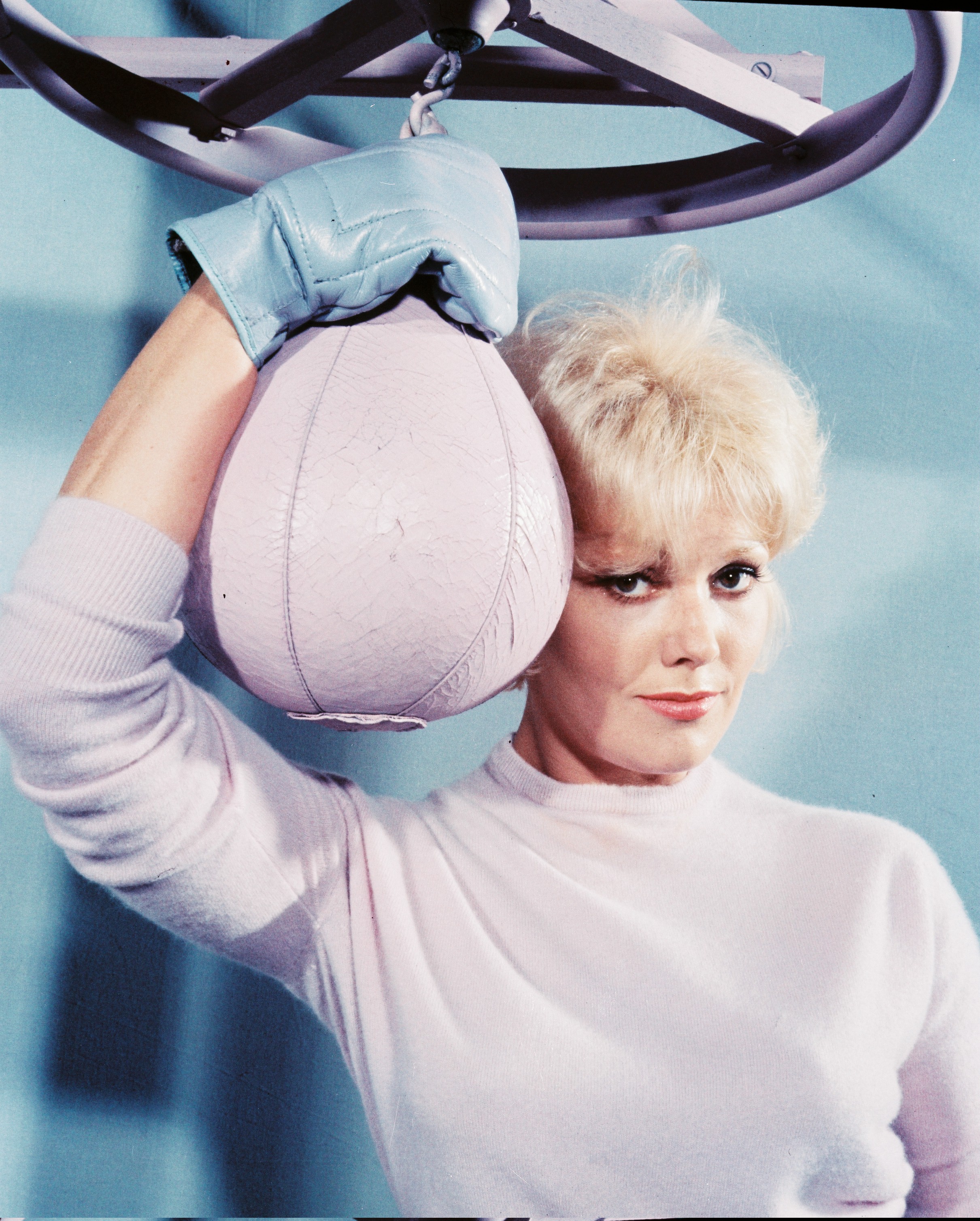 Kim Novak poses in a white wool sweater and blue boxing gloves beside a suspended punching ball in a studio portrait. | Source: Getty Images