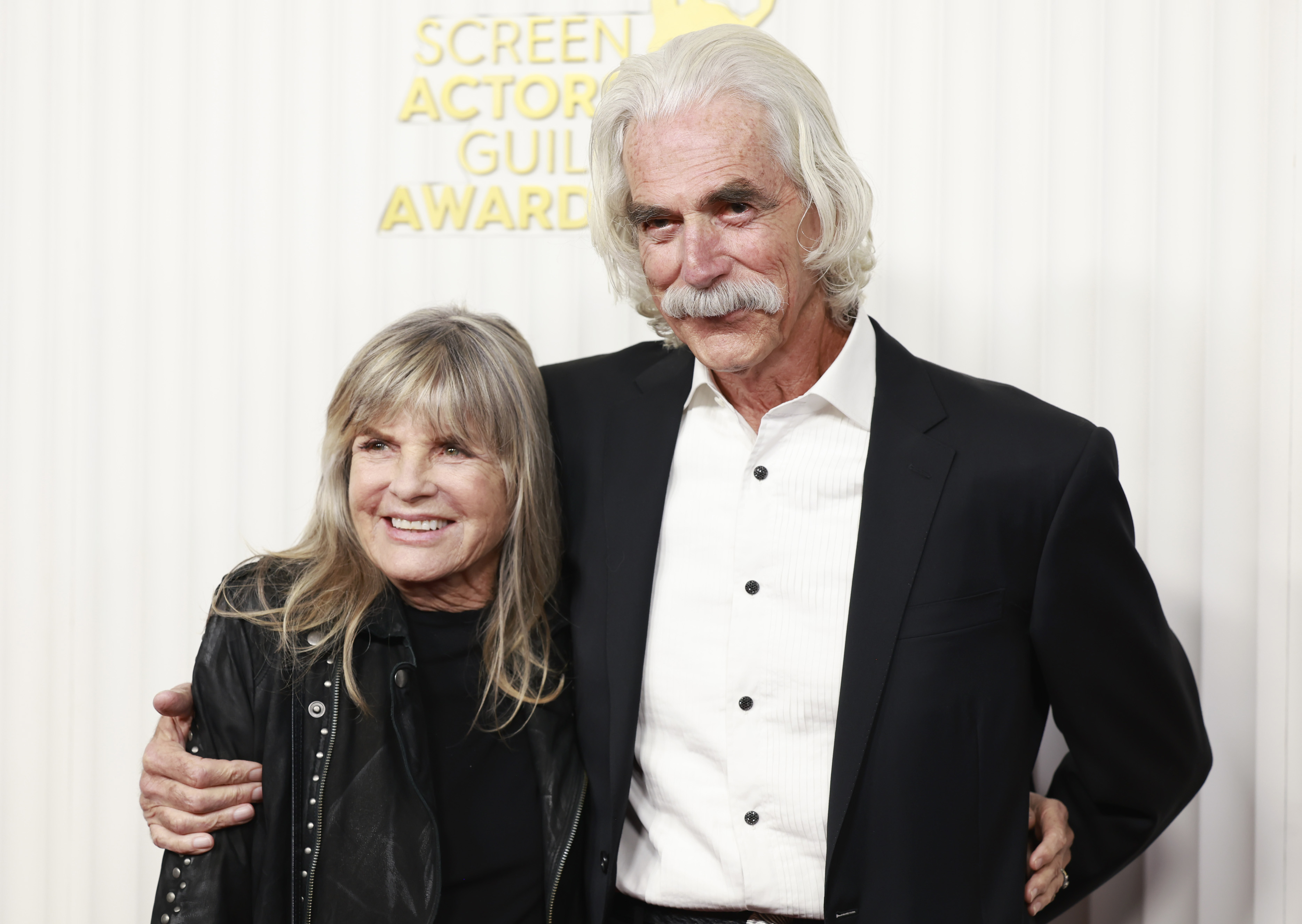 Katharine Ross and Sam Elliott shared a sweet, supportive moment on the red carpet at the 29th Annual Screen Actors Guild Awards on February 26, 2023, in Los Angeles, California. Sam stood sharp in an unbuttoned black suit jacket over an open-collared white dress shirt with dark buttons, his signature silver mustache and flowing hair stealing the spotlight. Embracing his arm with a beaming smile, Katharine brought an edgy vibe to the evening in a black studded leather jacket layered over a matching top. | Source: Getty Images