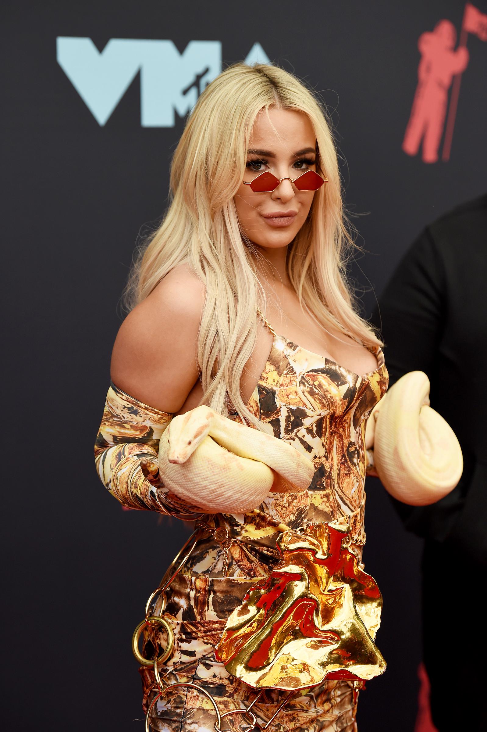 Tana Mongeau makes a cheeky statement in Newark, arriving in a gold, structural dress while carrying a yellow snake on the red carpet.