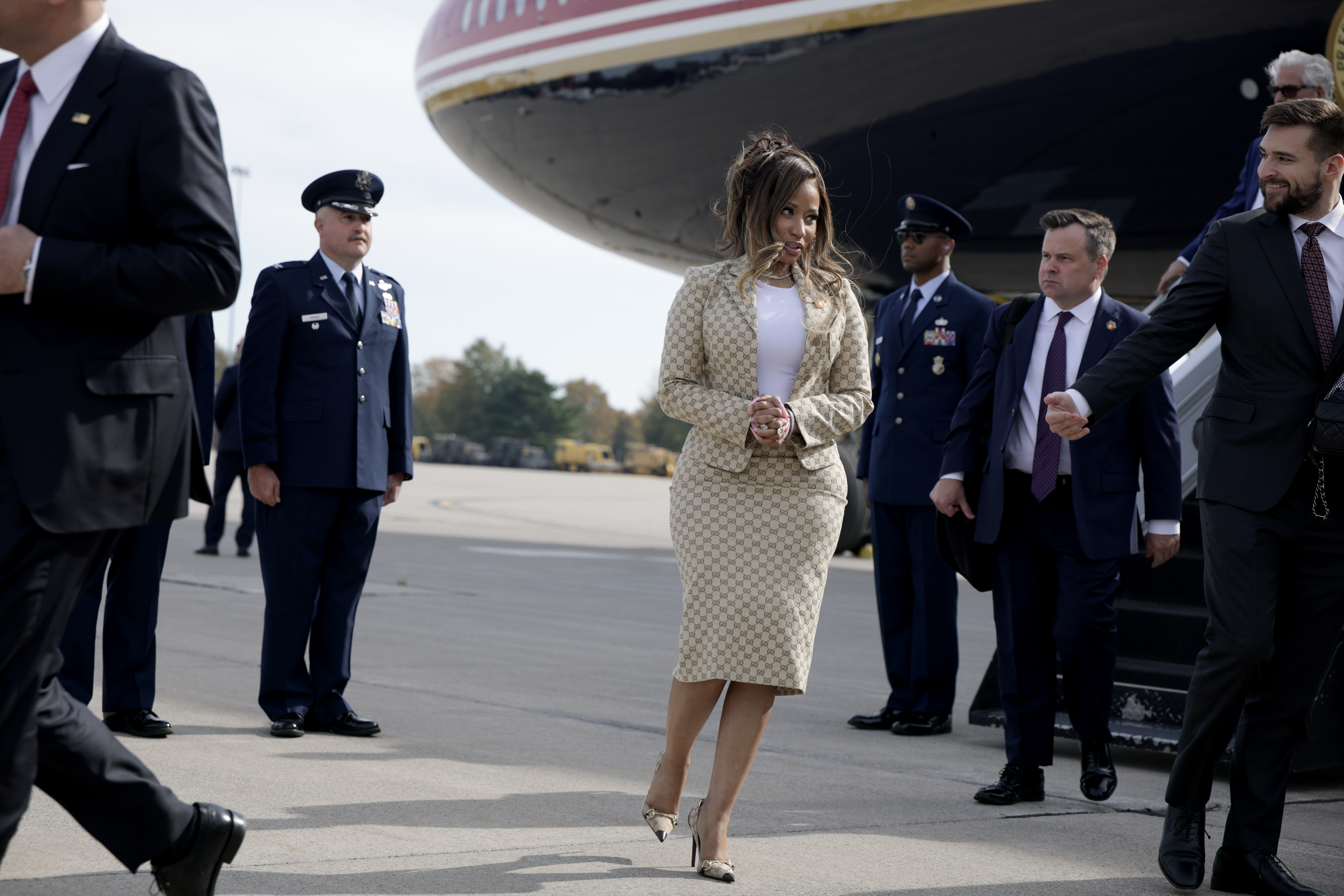 Nicki Minaj stands on the tarmac beside Air Force One, surrounded by uniformed military personnel and security staff. Her metallic pointed-toe heels and matching Gucci skirt complete the carefully coordinated look. | Source: Getty Images